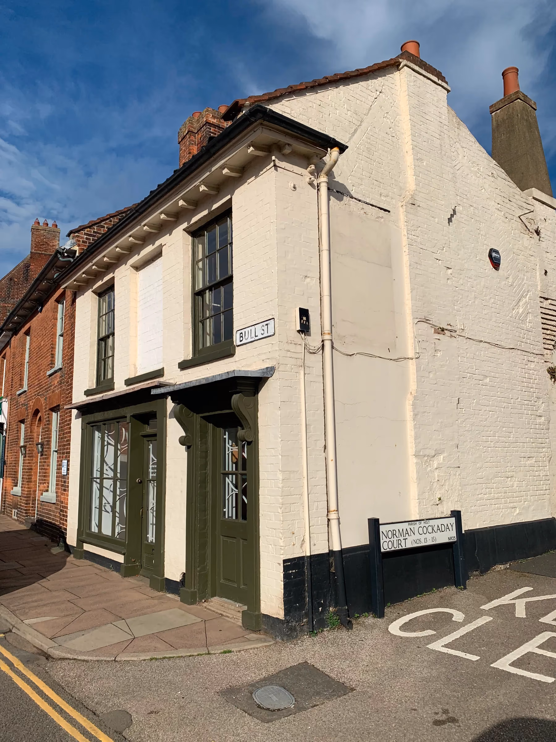 Front elevation before work, with cream painted walls and a dark green shopfront on the corner