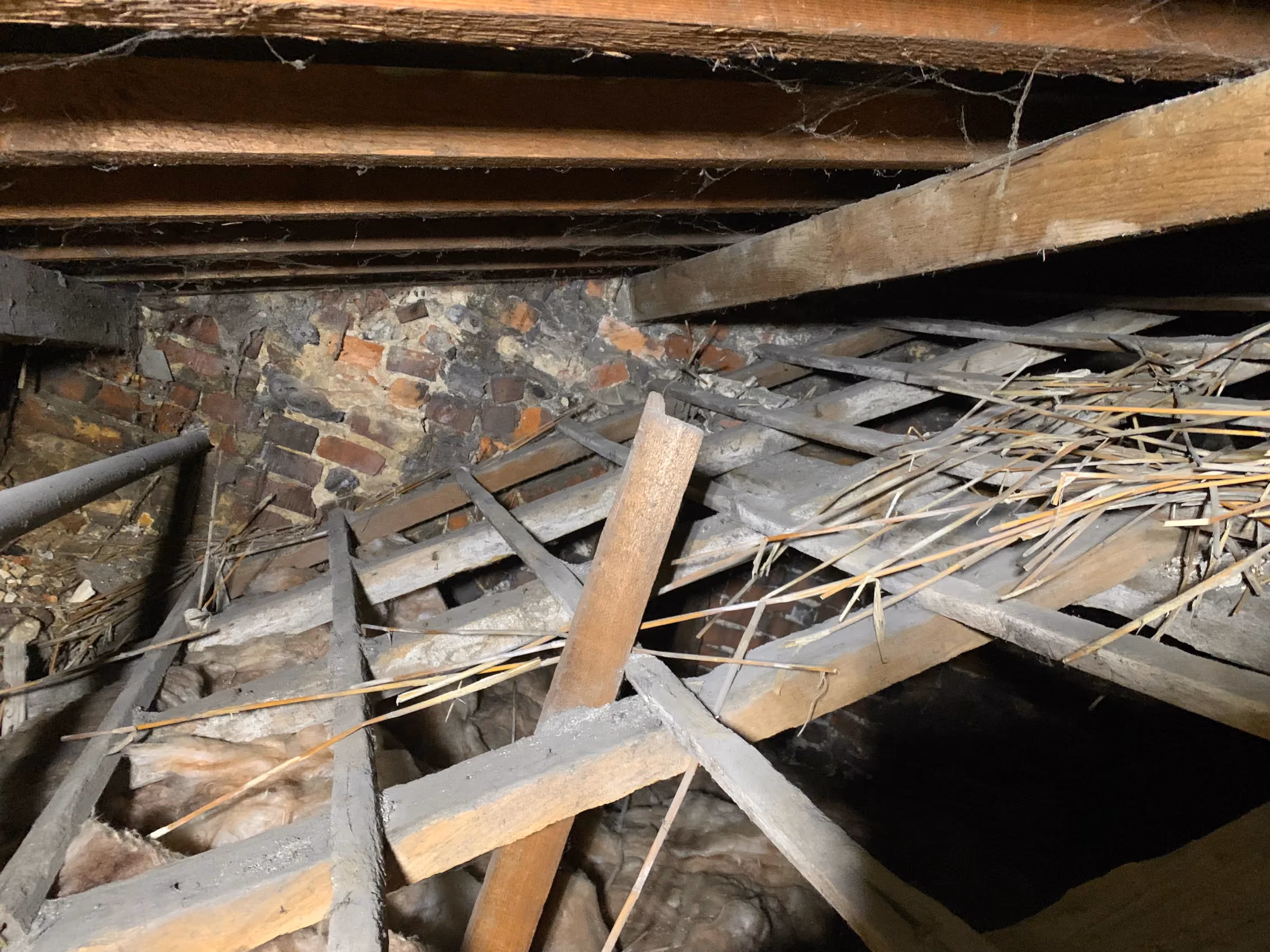 Old roof members in the attic with remnants of thatch still lying over the battens