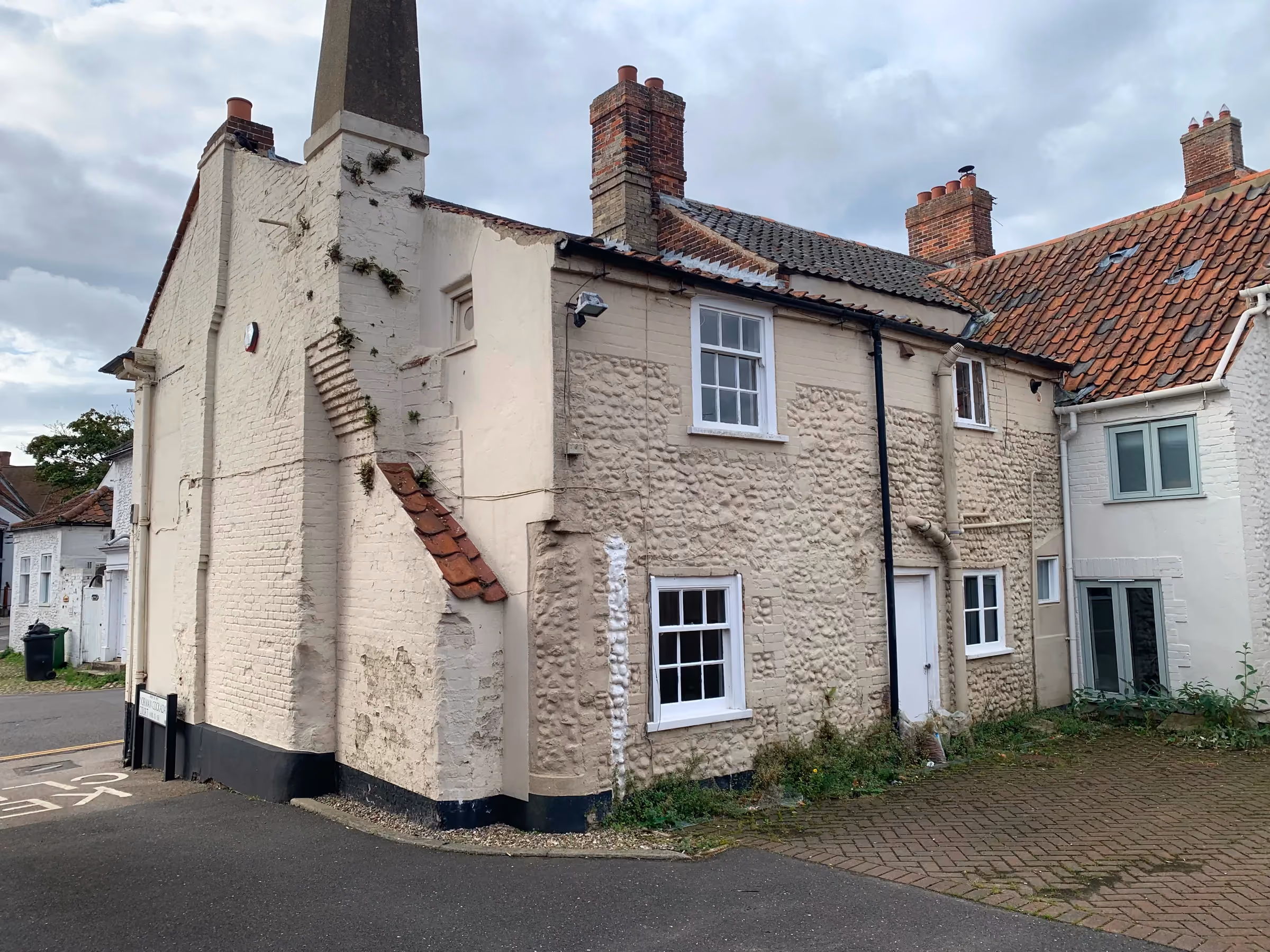 Painted corner elevation of the Georgian building in Holt before restoration, with weeds along the base of the walls