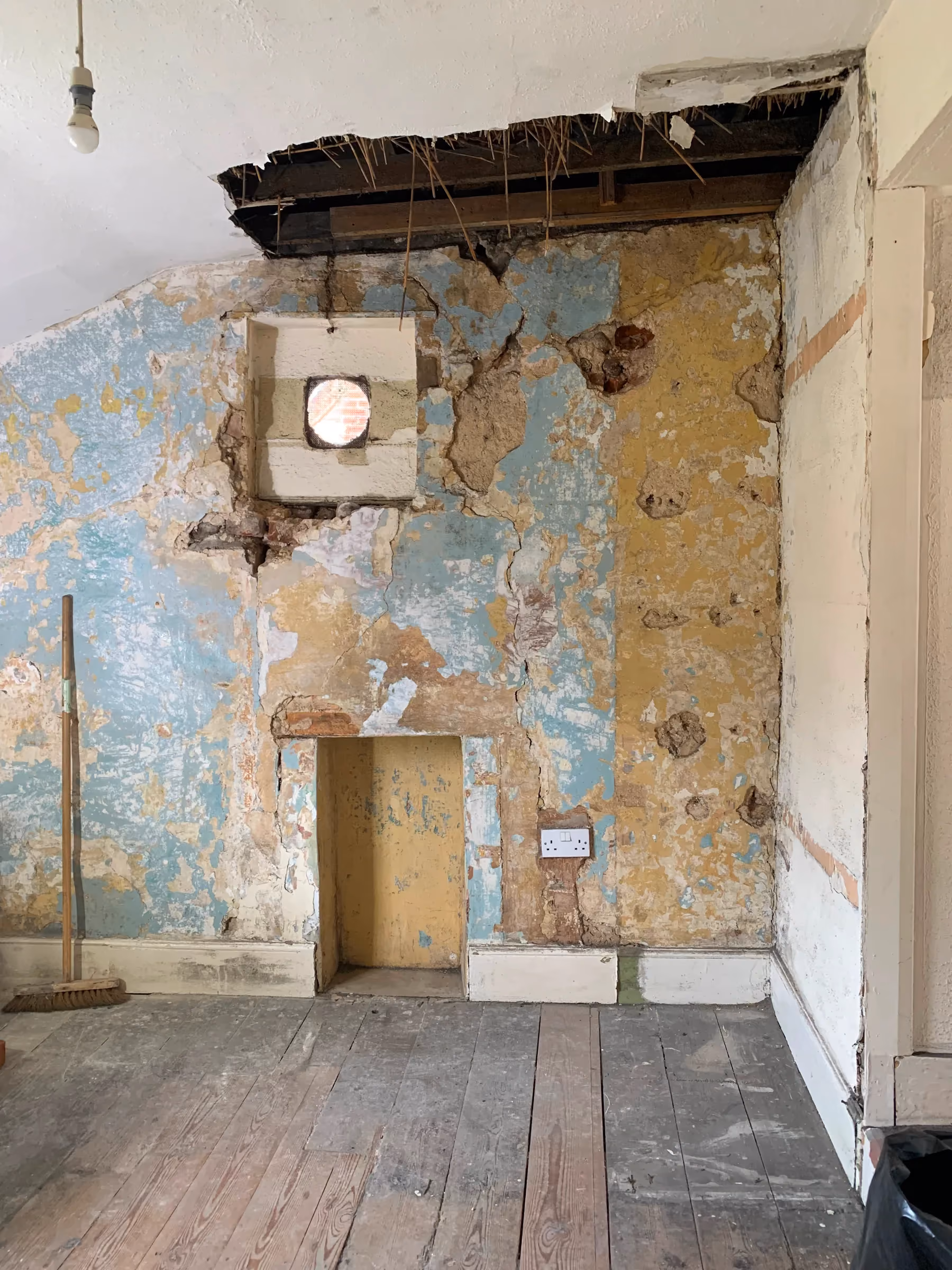 Back room with its gypsum plaster stripped, revealing old wallpaper, brickwork and lime plaster