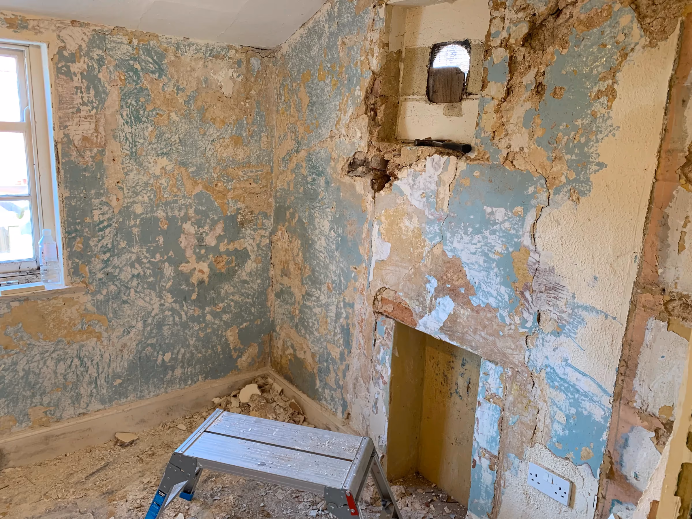 Stripped walls in the corner of the back room, with patches of old wallpaper and plaster
