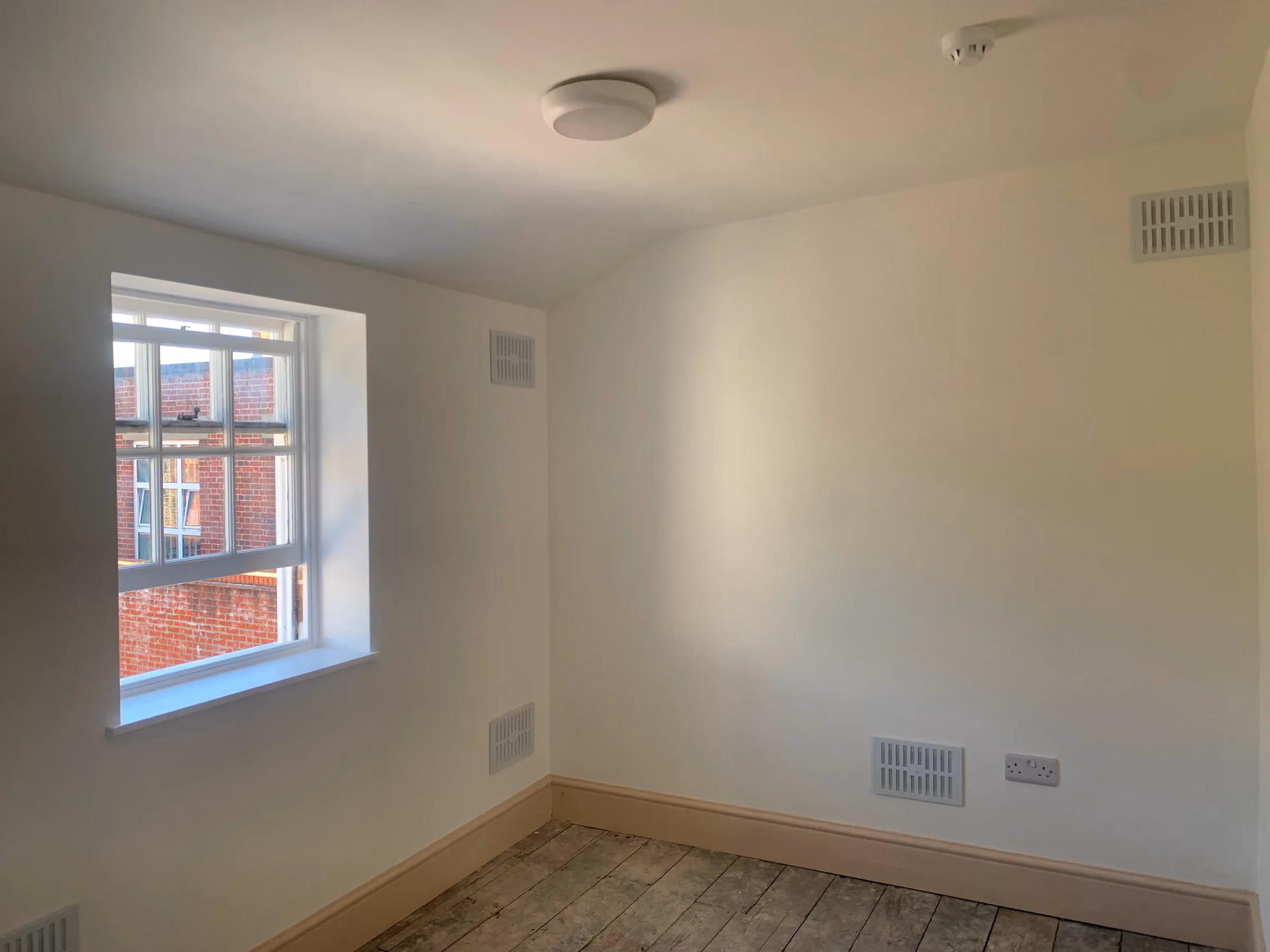 Finished back room with smooth plastered walls, a sash window and new wall vents