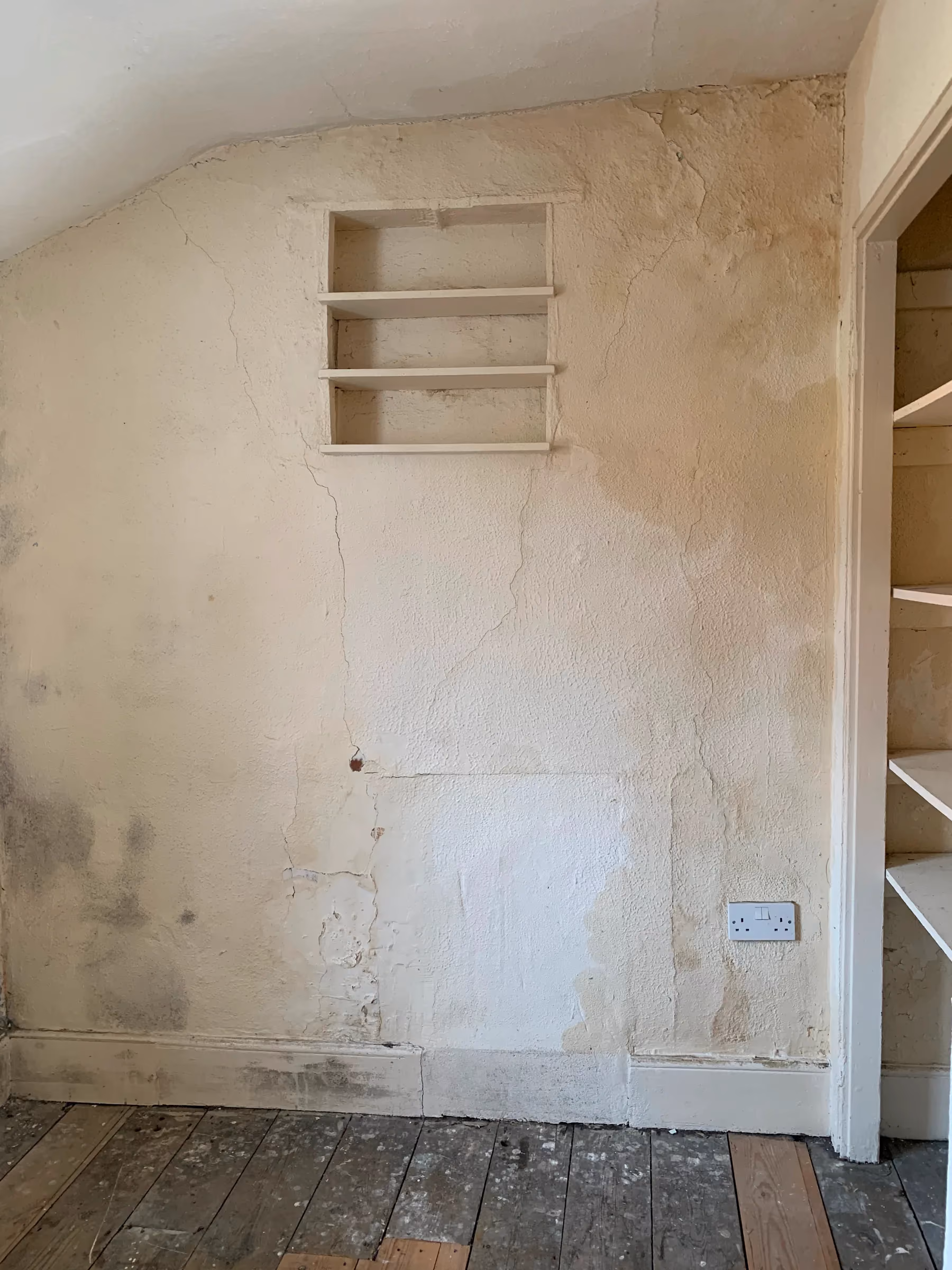 Damp stained wall with patches of mould and cracked paint beside a built in cupboard