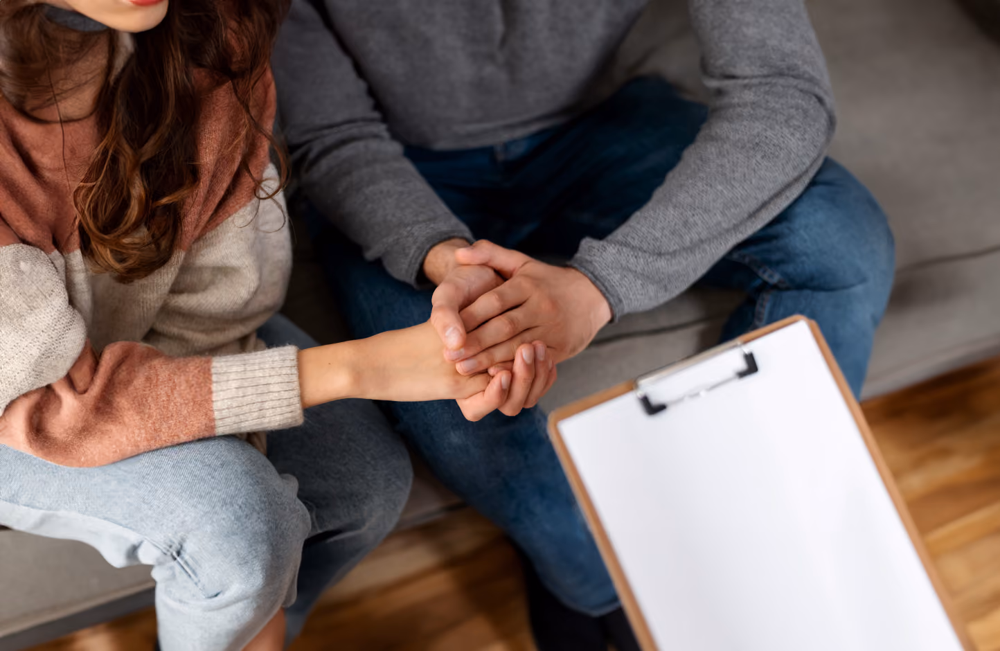 A man and woman sitting on a couch holding hands.