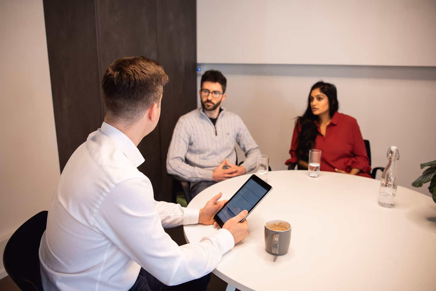 A group of people sitting around a table with a tablet.