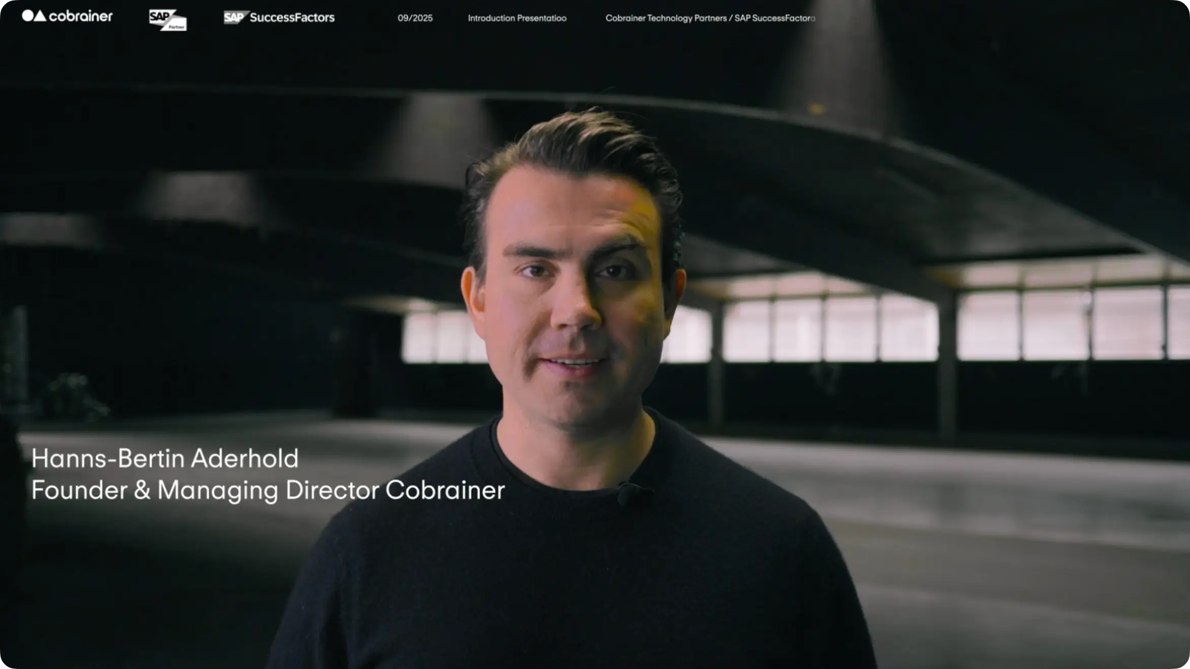 Hanns stands in a large industrial space with dim lighting and windows in the background; text reads 'Hanns-Bertin Aderhold Founder & Managing Director Cobrainer.'