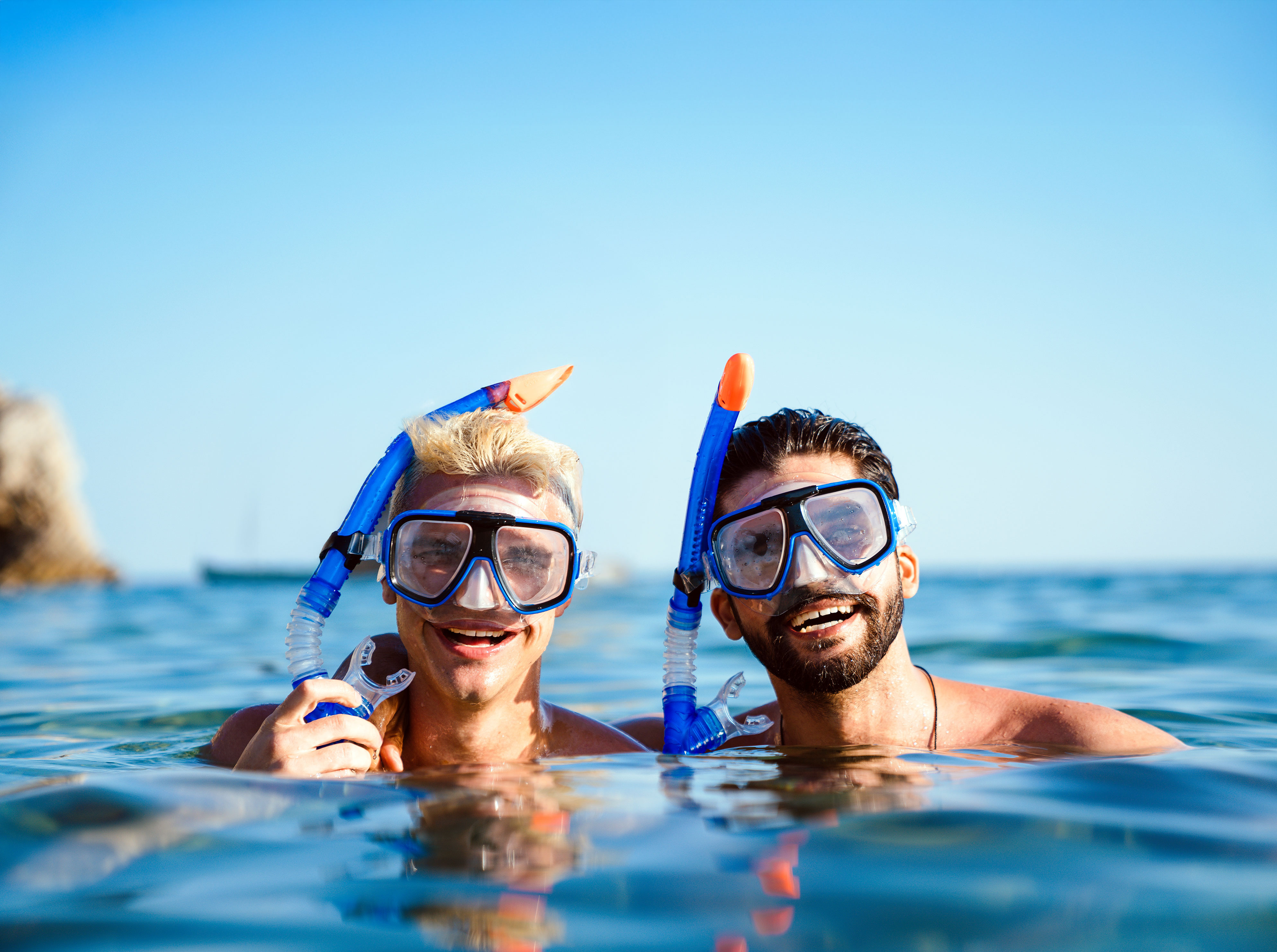 Two men smiling and wearing snorkeling masks with snorkels in the ocean on a clear sunny day.