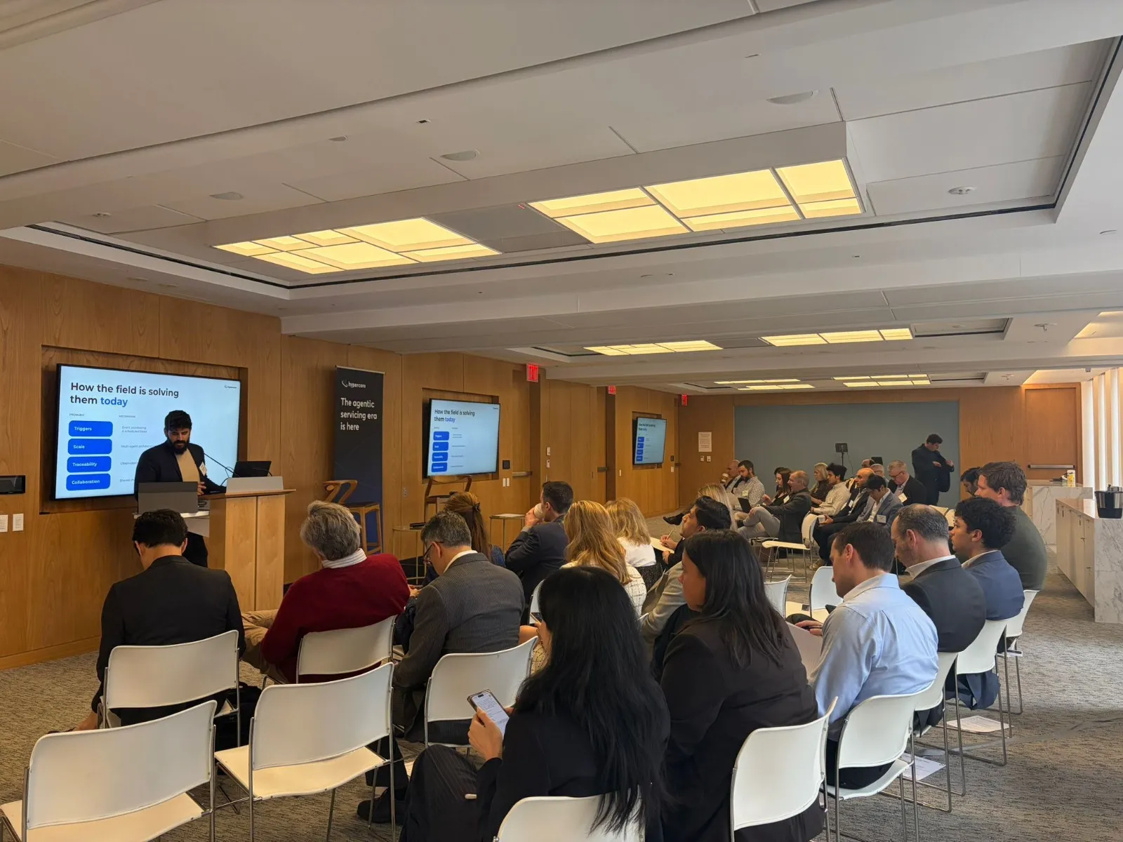 Man presenting in a conference room with audience seated, slides show challenges and solutions.