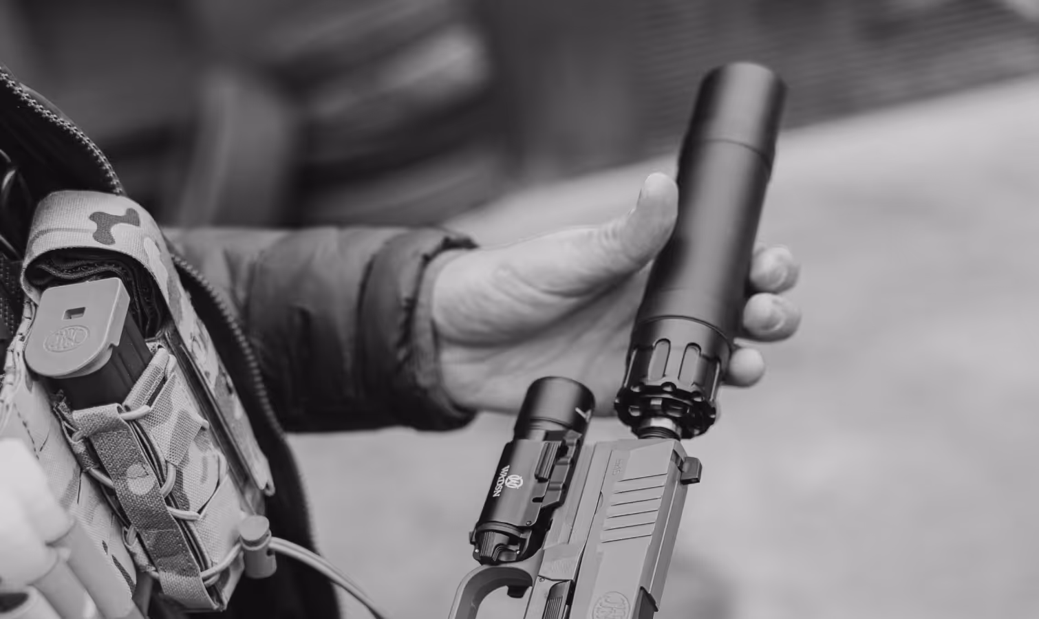 Hand attaching a silencer to the barrel of a pistol held in the other hand.