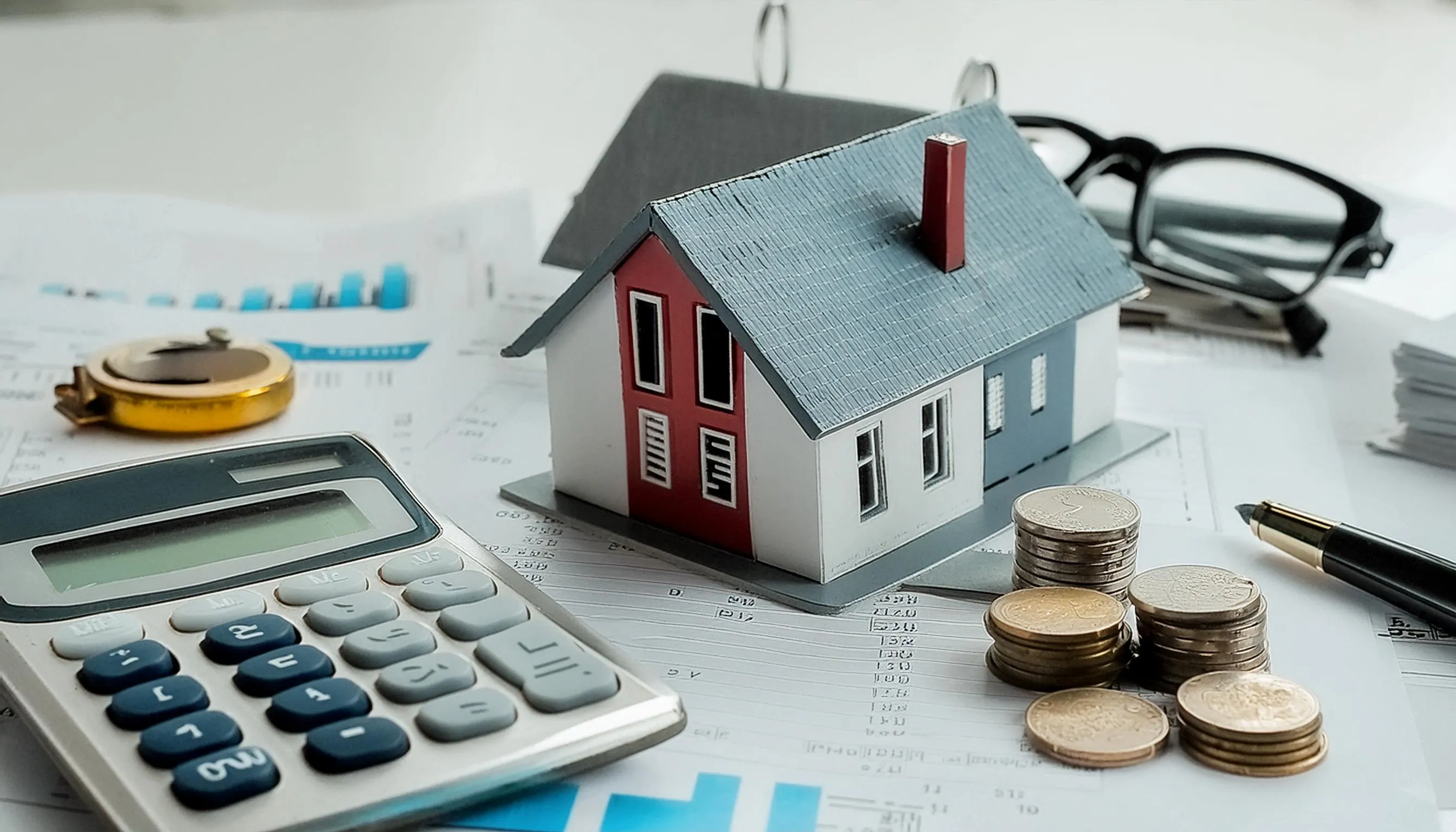 Maquette de maison avec calculatrice, pièces de monnaie et documents financiers, symbolisant les régimes fiscaux de l'immobilier locatif.