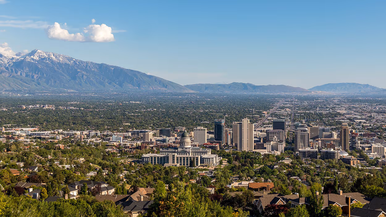 Elevated city view with mountains in the background on a clear day, showcasing a mix of urban buildings and greenery.