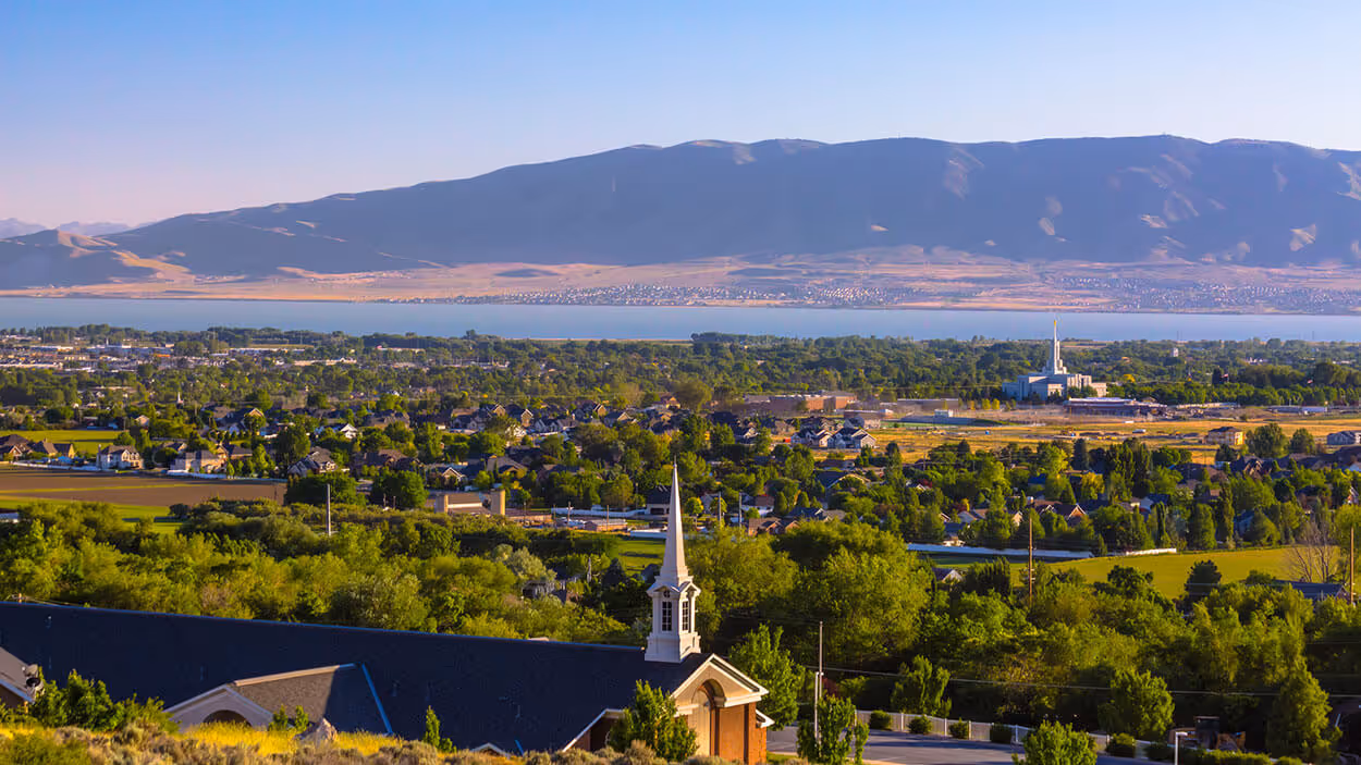 A scenic view of a suburban area with houses, trees, and a distant mountain range under a clear blue sky.