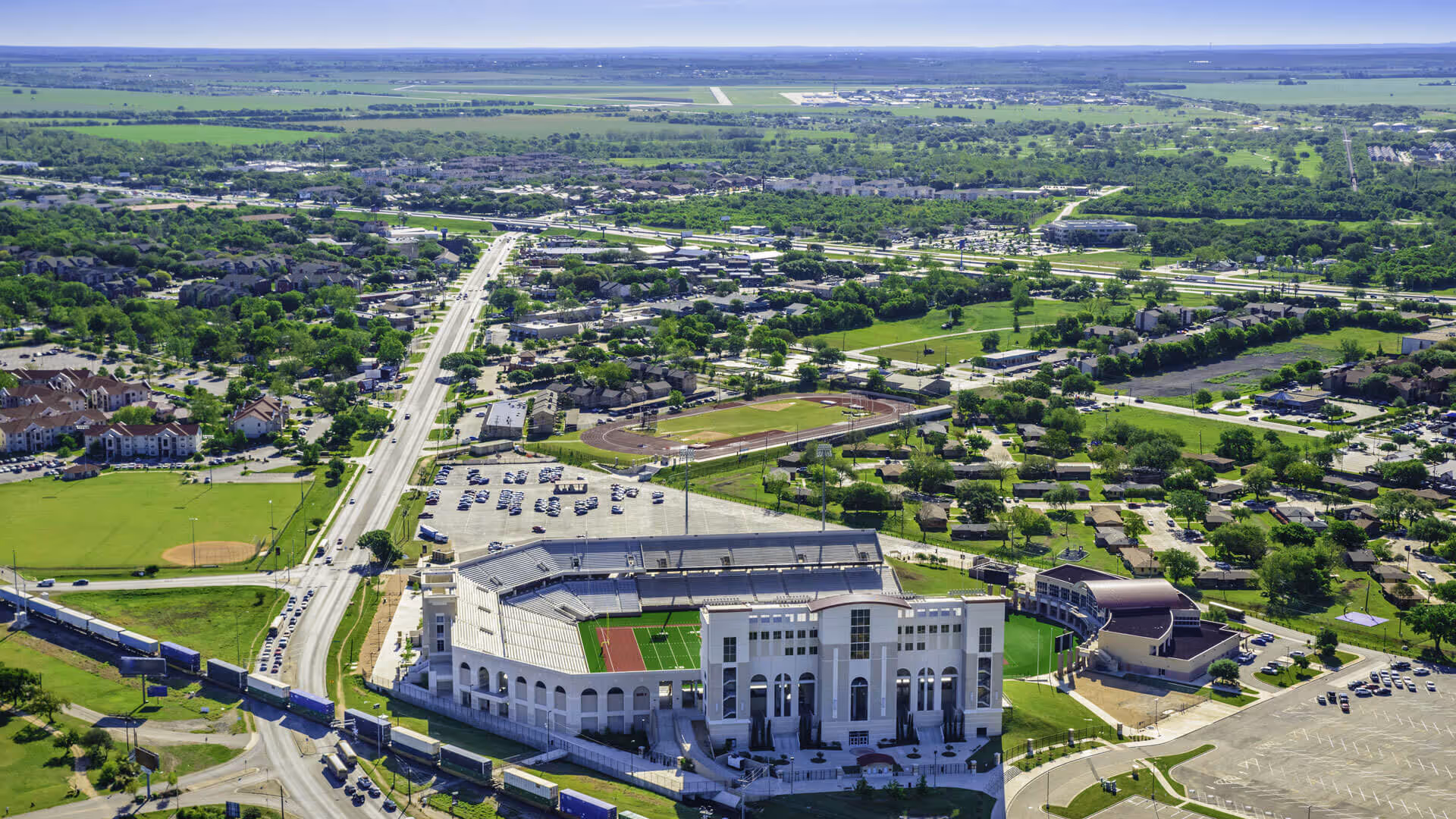 Aerial view of a large football stadium surrounded by roads, parking lots, buildings, and green fields.