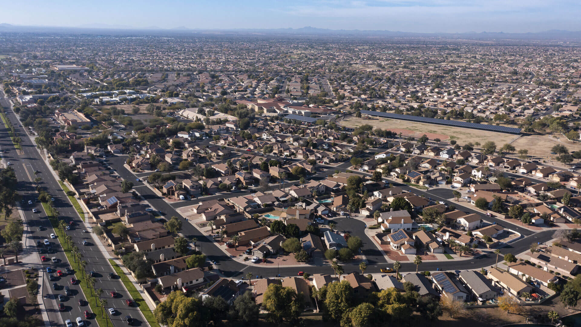 Aerial view of a sprawling suburban neighborhood with houses, streets, and distant mountains under a clear sky