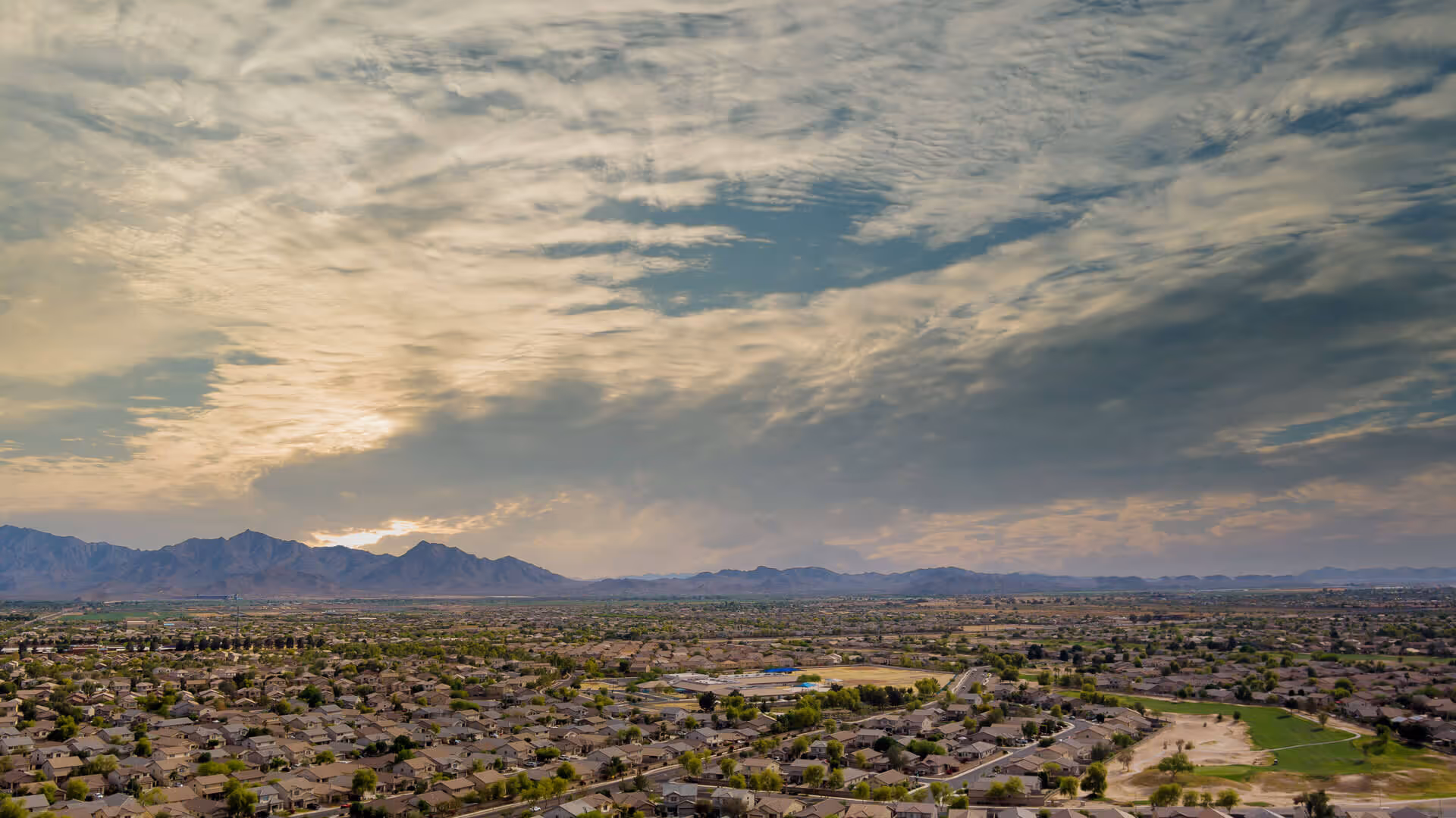 Aerial view of a suburban neighborhood with mountains in the distance under a cloudy sky at sunset.
