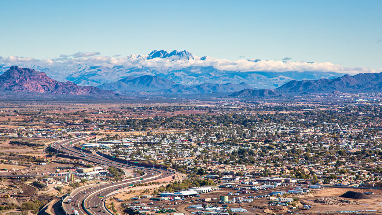 Aerial view of a city with a highway, scattered buildings, and distant mountains under a clear sky.