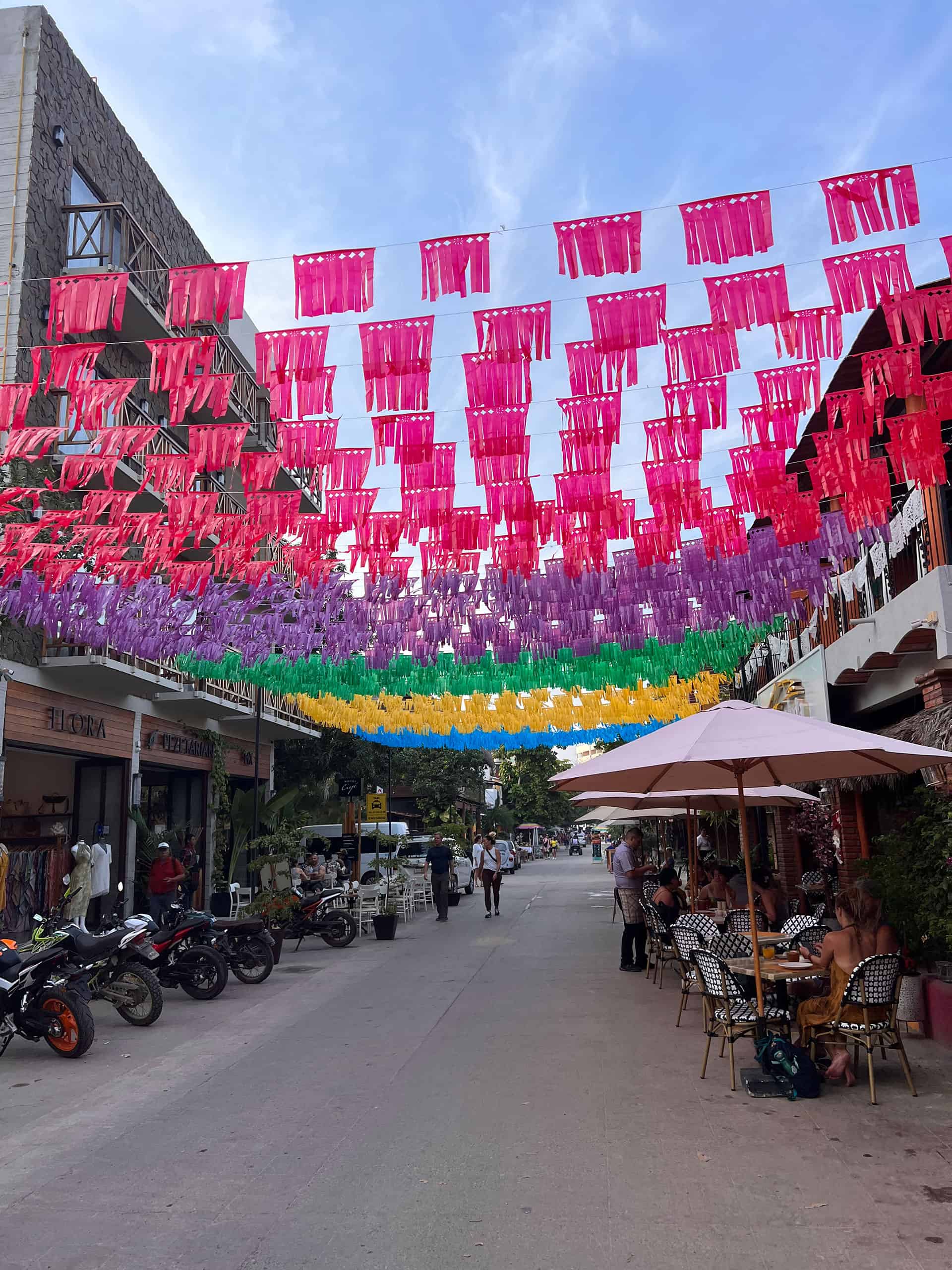 Av. Tercer Mundo with festive flags strung across the street between two restaurants.