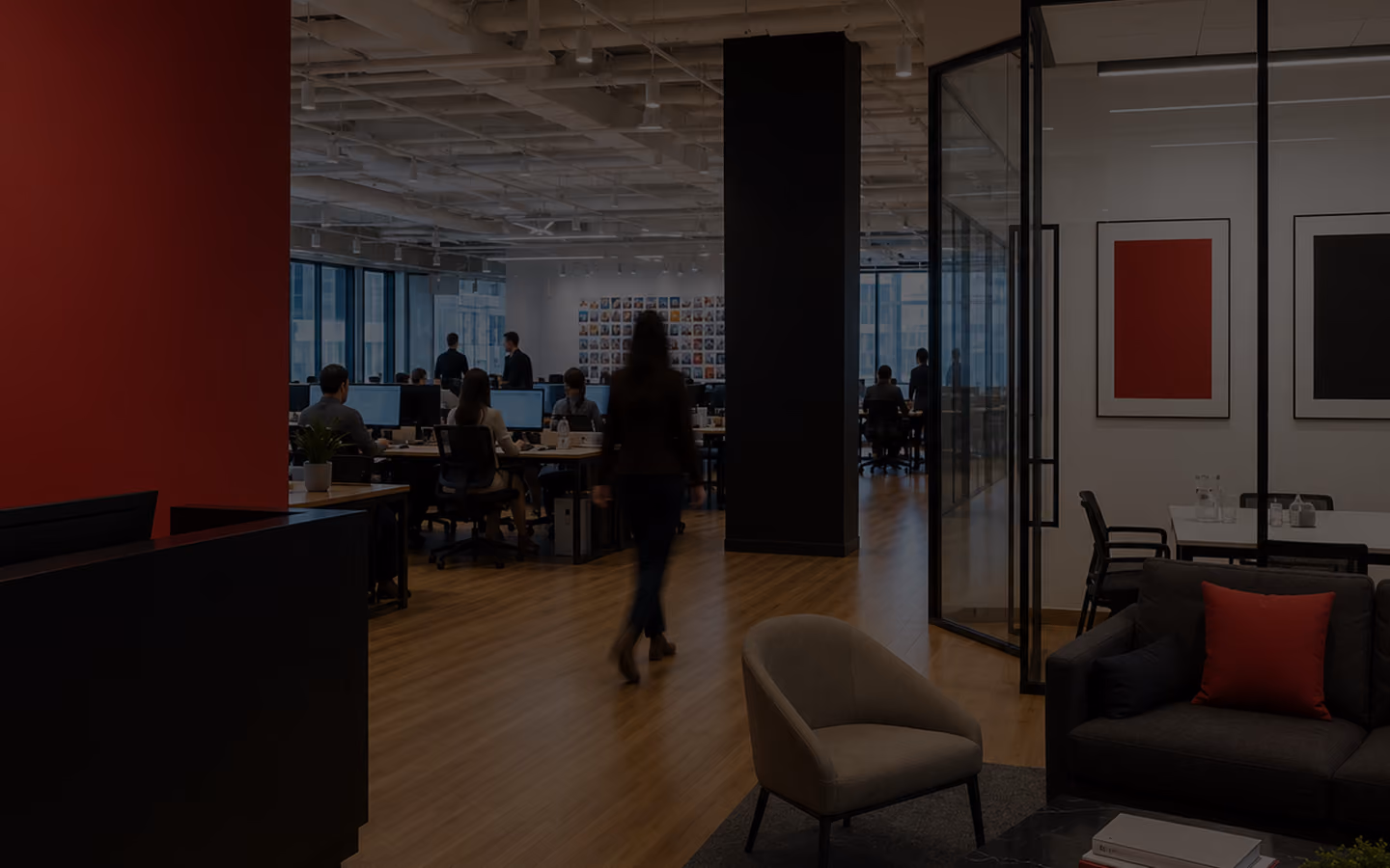 Modern office with people working at desks, a woman walking, and a glass-walled conference room.