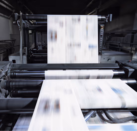 Newspapers rapidly moving through a printing press in a factory setting.