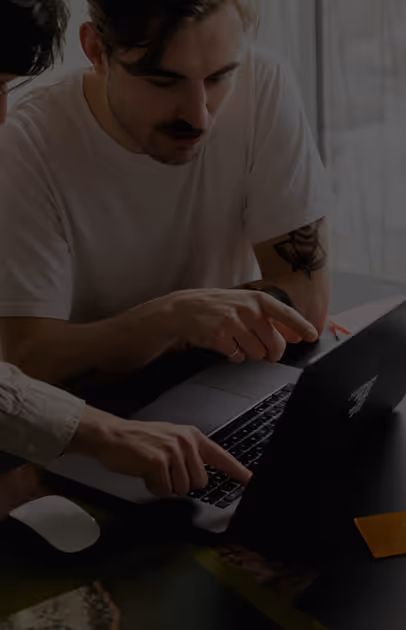 Two people pointing at a laptop screen while discussing work.