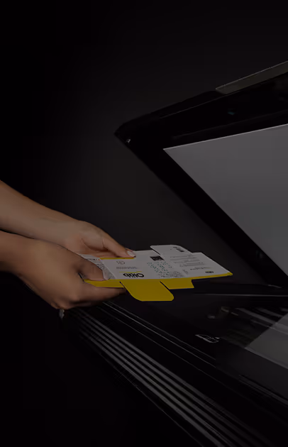 Two hands placing a yellow and white printed control card into a flatbed scanner against a black background.