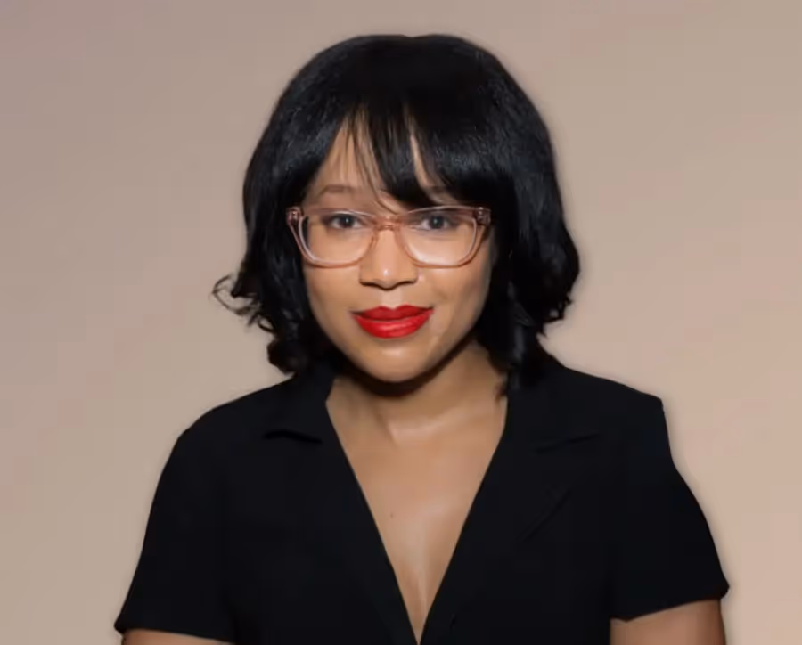 Smiling woman with black hair wearing pink glasses, red lipstick, and a black top.