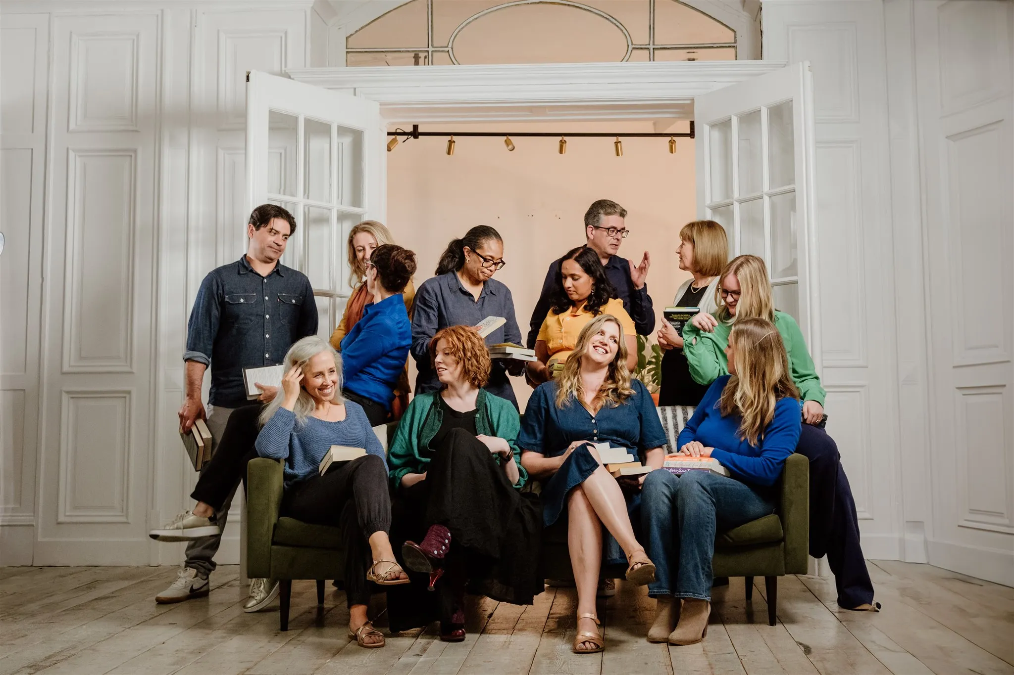 Group of diverse adults sitting and standing in a bright room, holding books and engaging in conversation.