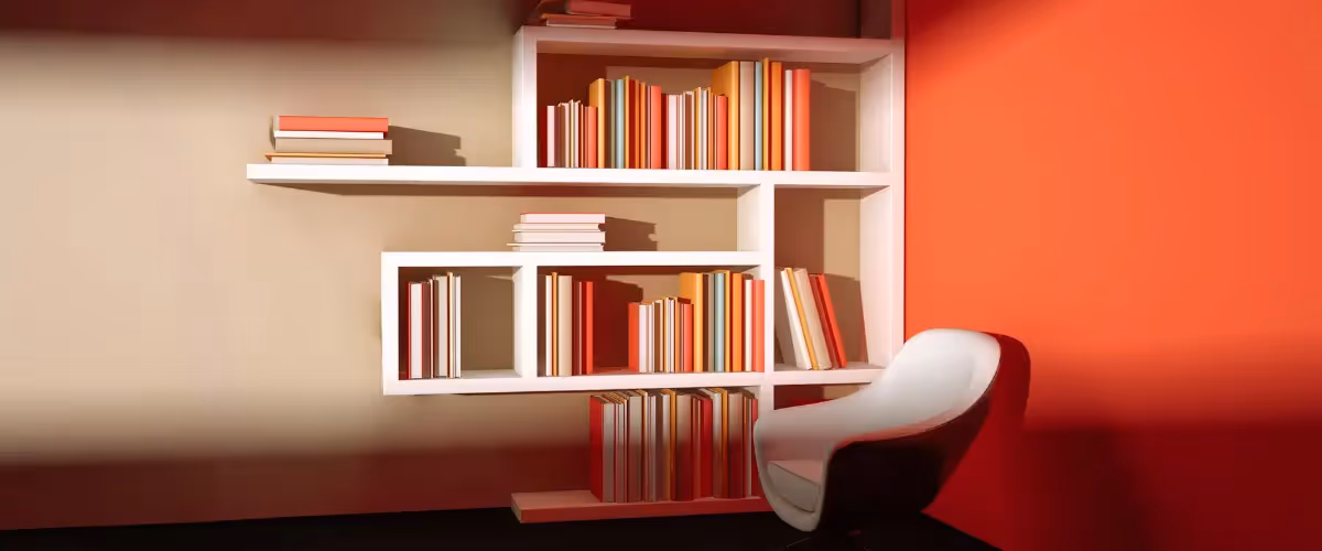 A bookshelf stacked with books of varying sizes in shades of orange and white, with a white armchair sitting in front.