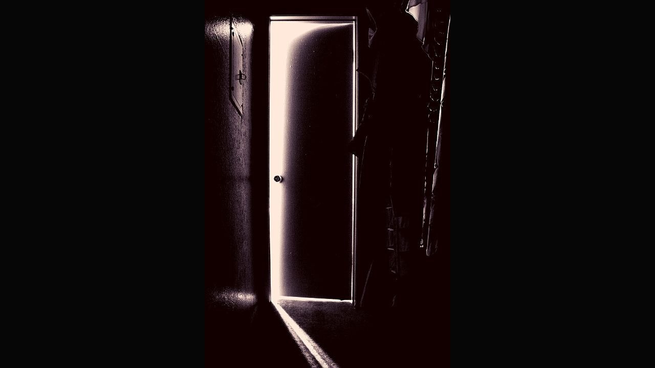 A slightly open door, showing a sliver of light in an otherwise very dark corridor.