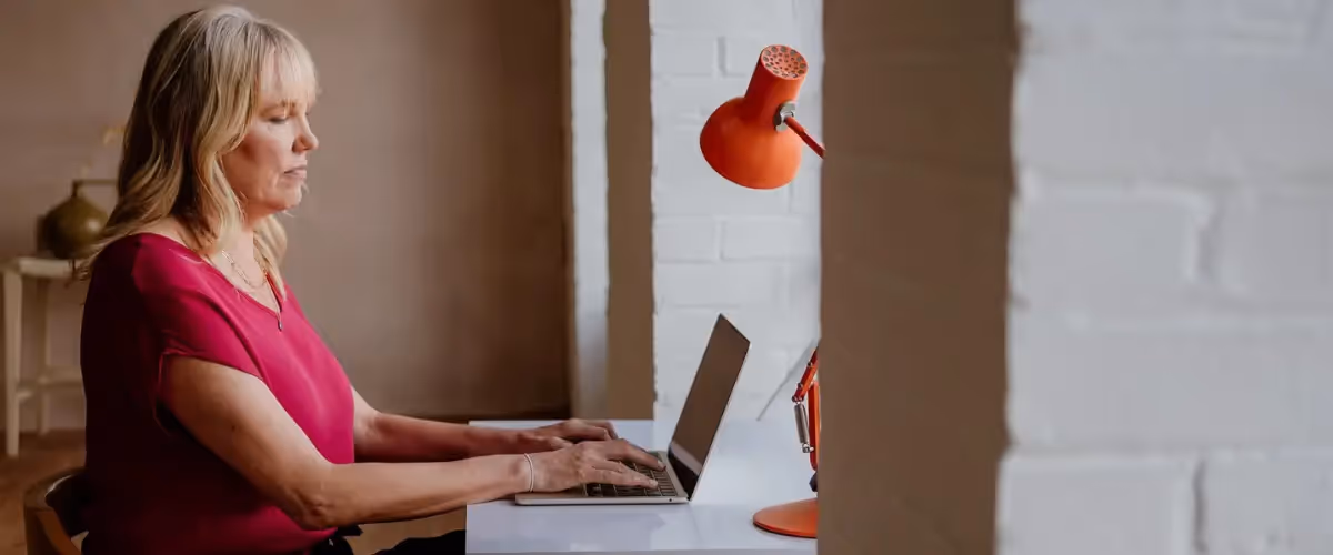 Author and writing coach Tara Conklin types on a laptop beside an orange lamp.