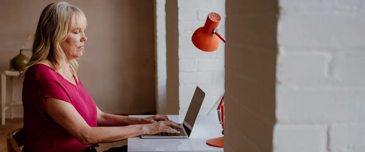 Author and writing coach Tara Conklin types on a laptop beside an orange lamp.