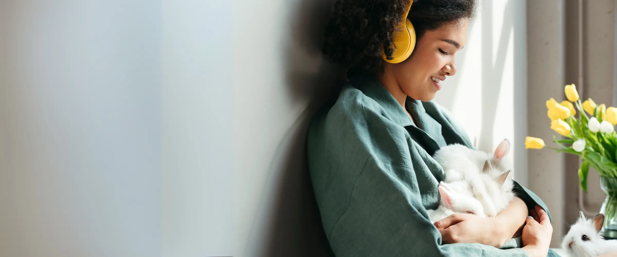 A woman wearing headphones hugs some baby bunnies.