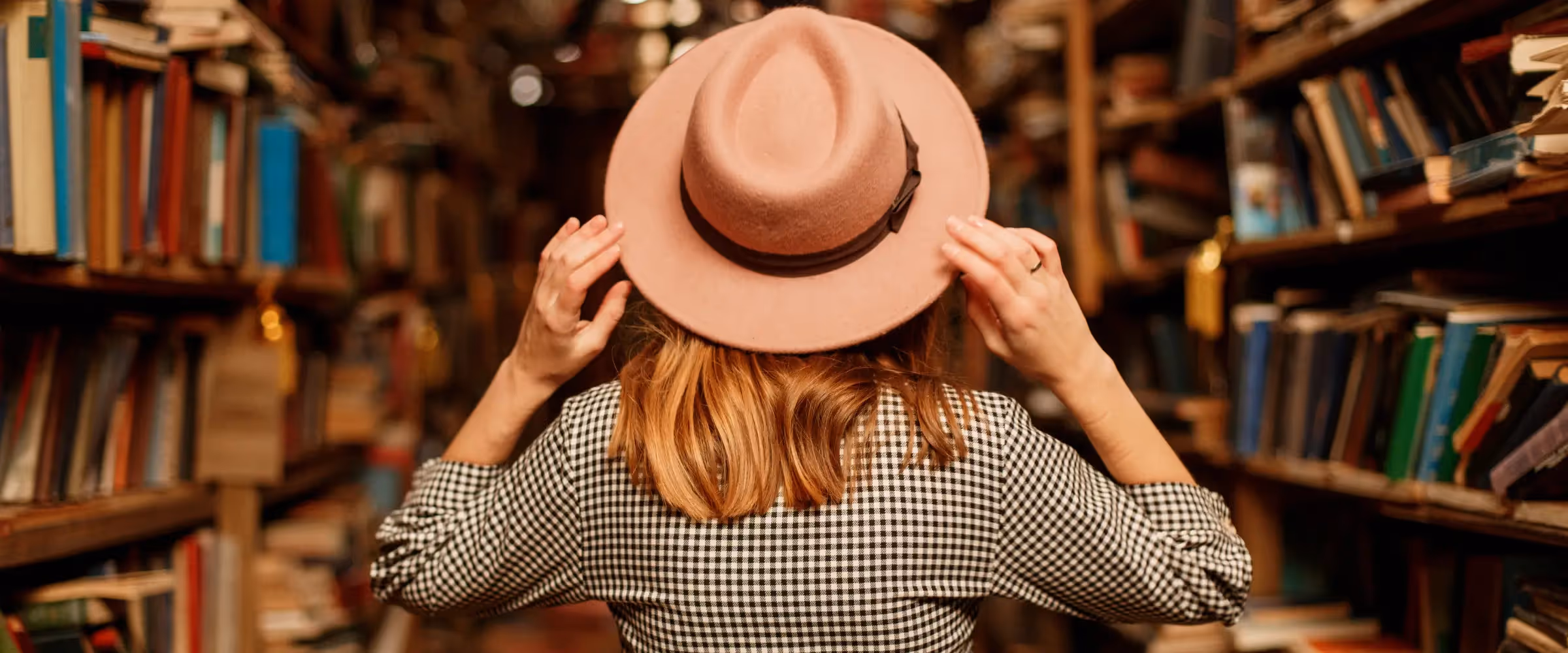 A woman wearing a hat stands inside a packed bookstore.