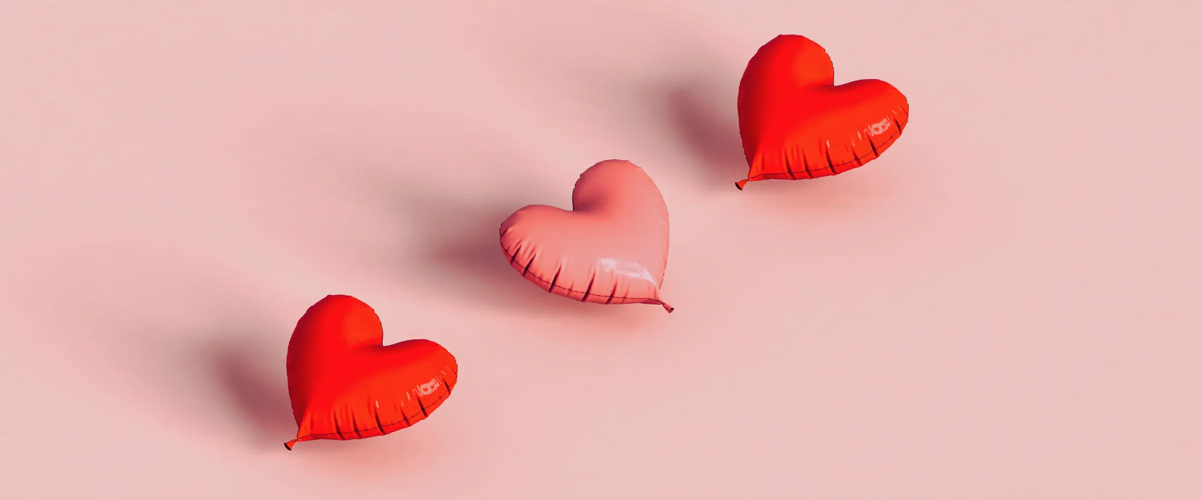 Three heart-shaped balloons in pink and red.