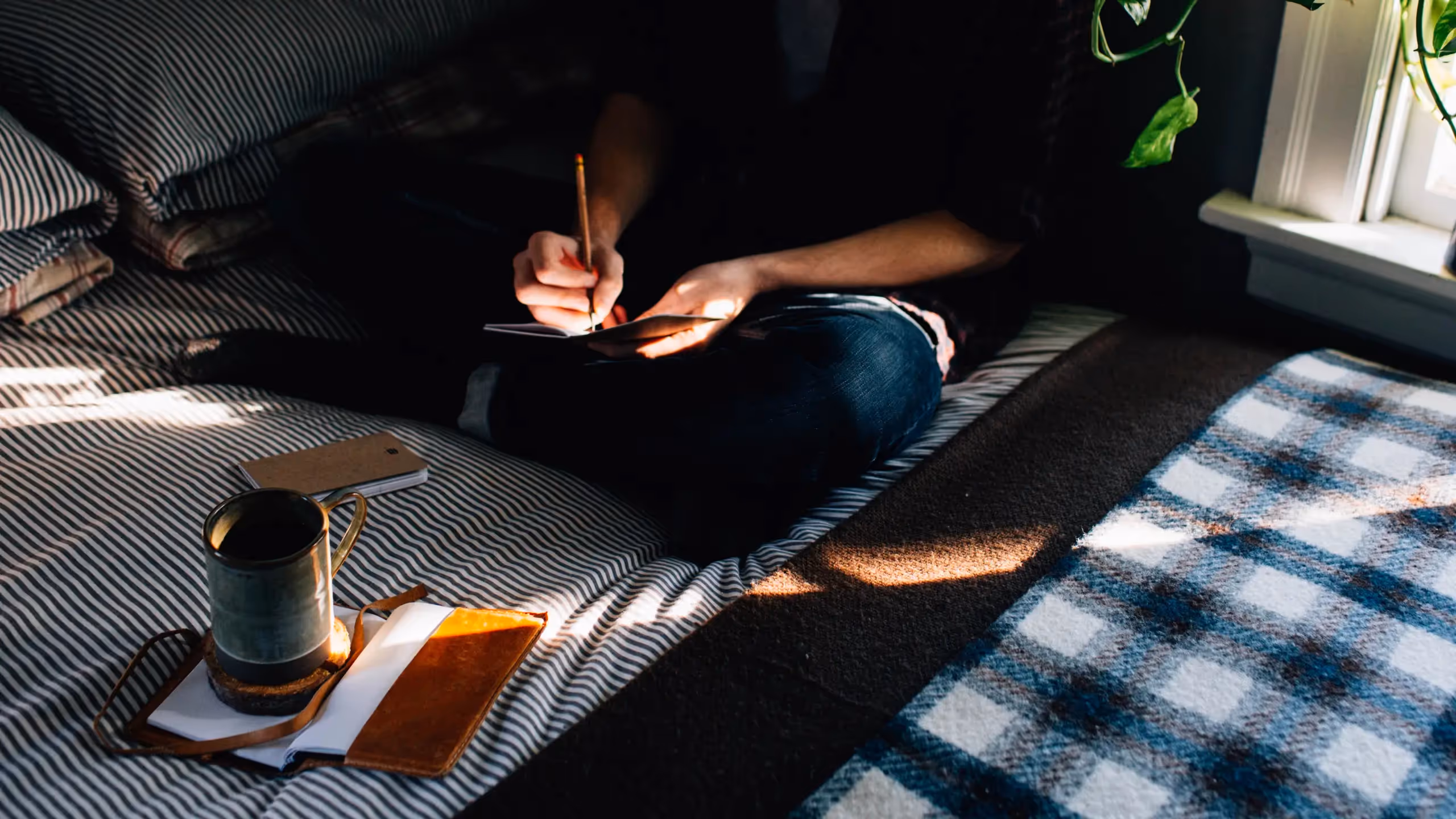 A figure sits cross-legged on a bed, writing in a notebook.