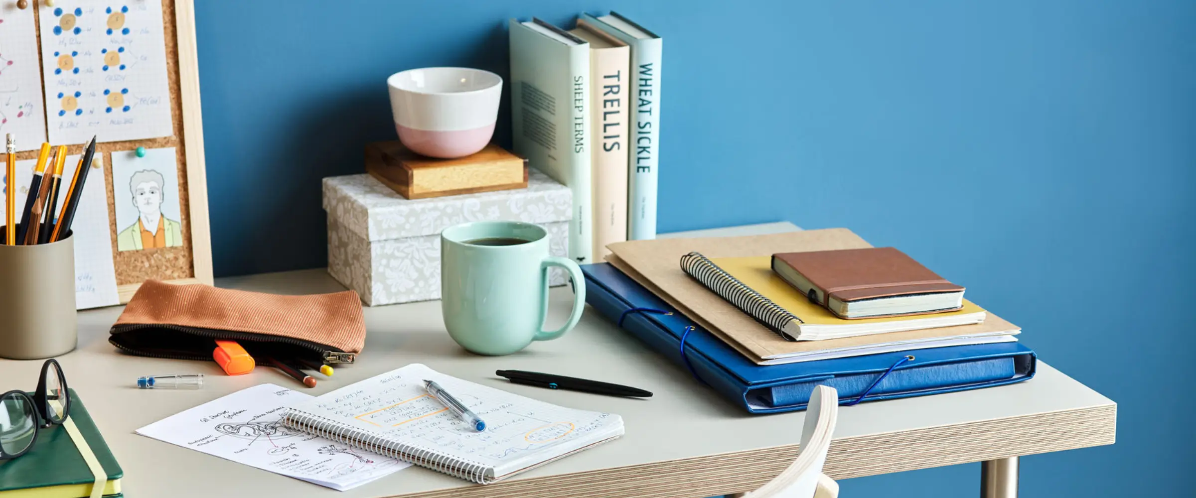 A desk with books, notepads, pens, and a cup of coffee.