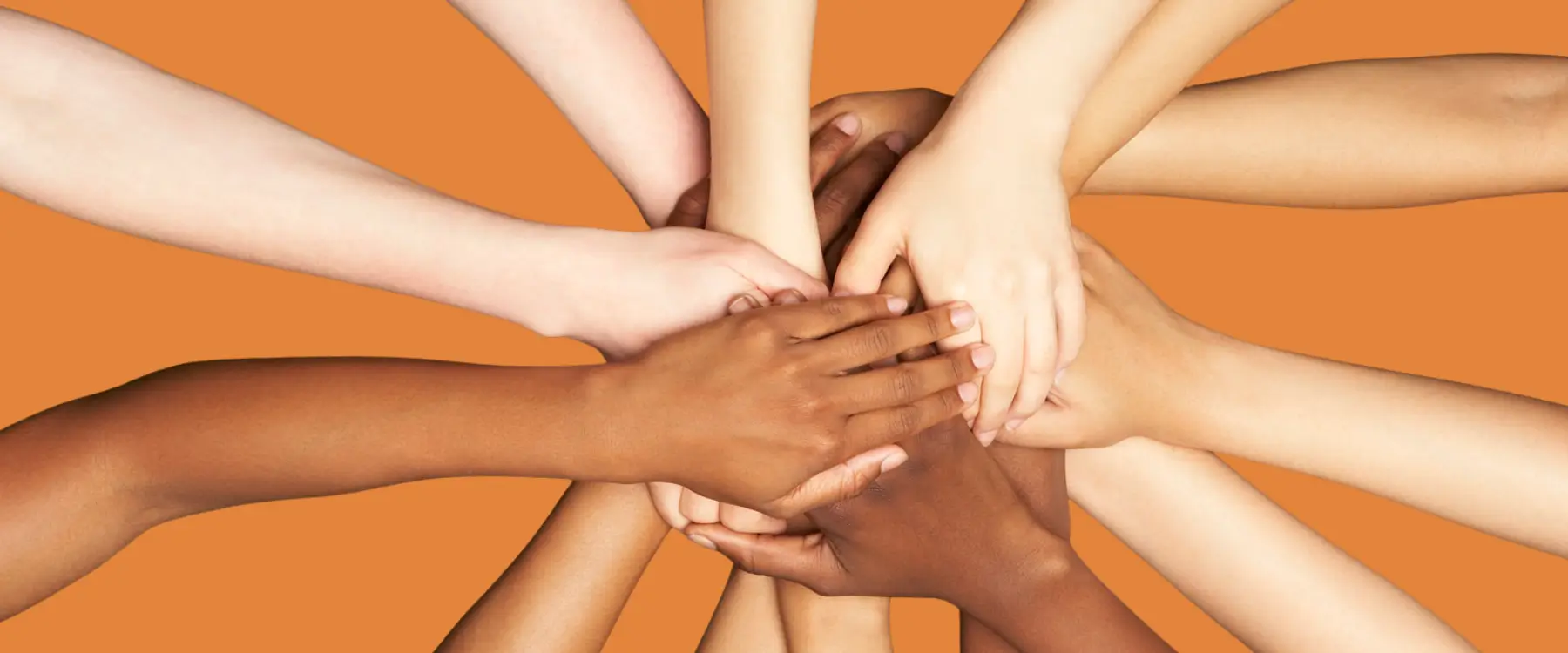 Overhead view of seven people of varying skin tones stacking their hands on top of each other in a teamwork gesture.