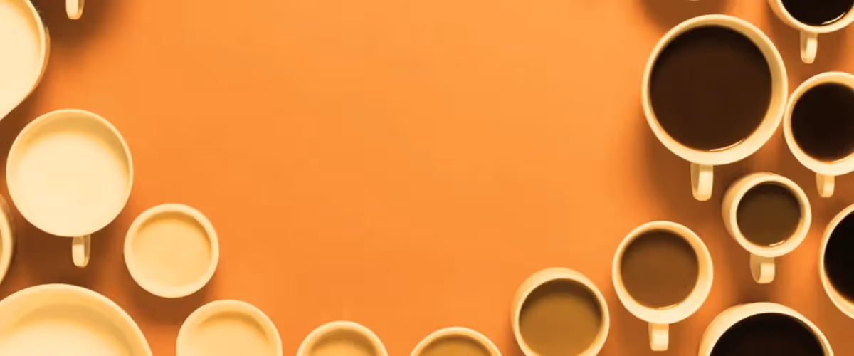 An overhead shot of lots of china cups containing different hot drinks on an orange background.