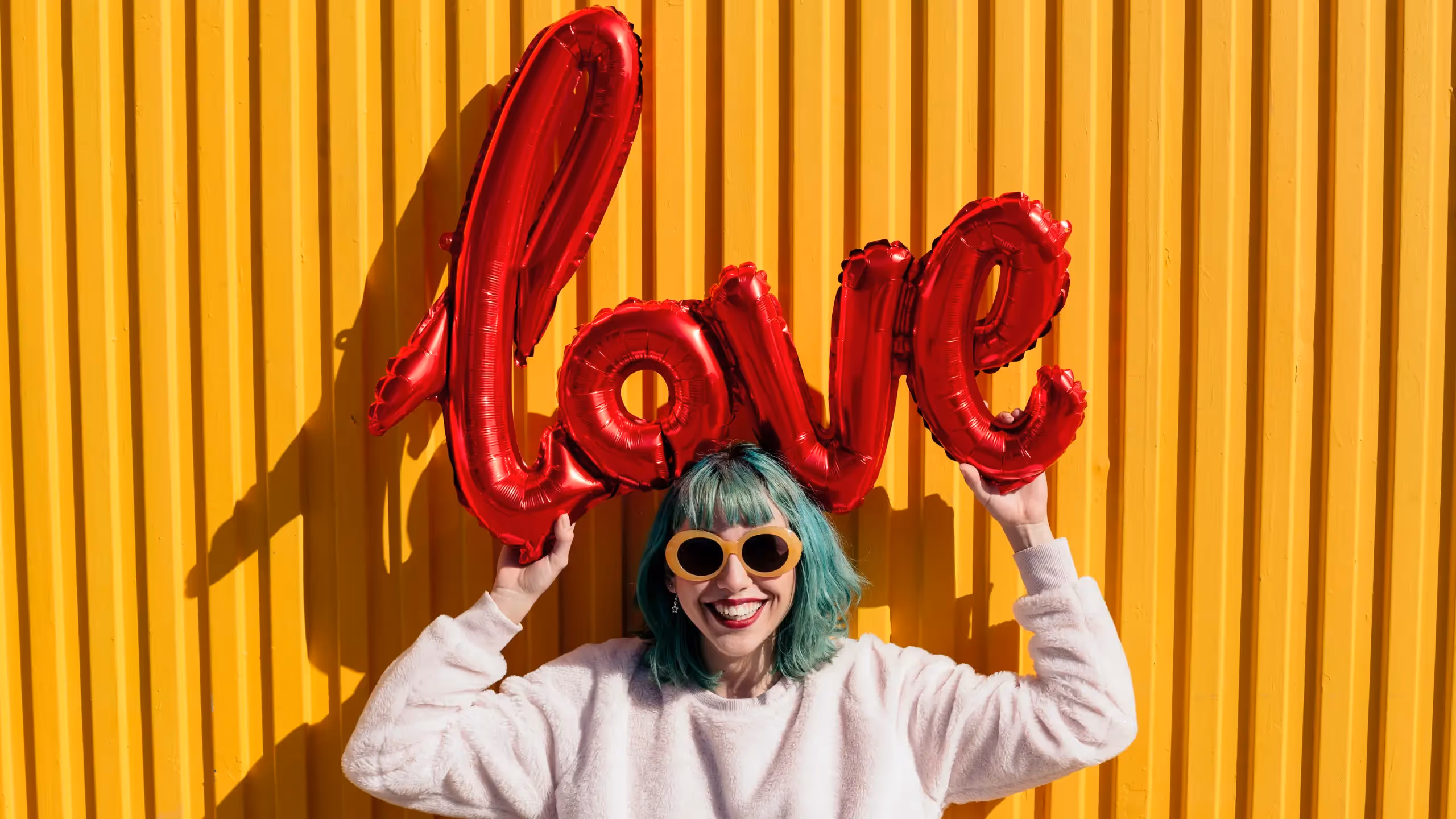 Teenager with green hair holds a sign above her head that says 'love' to celebrate top 25 YA romance books.