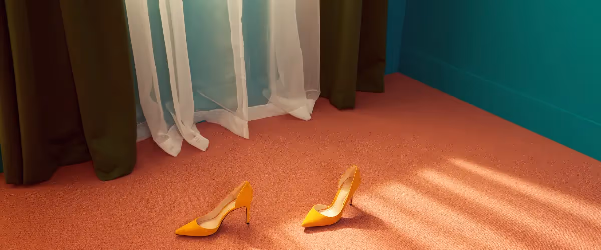 A pair of yellow high heels on an orange carpet and green walls.