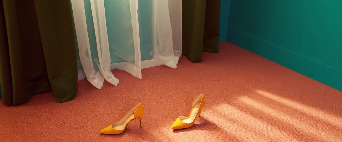A pair of yellow high heels on an orange carpet and green walls.