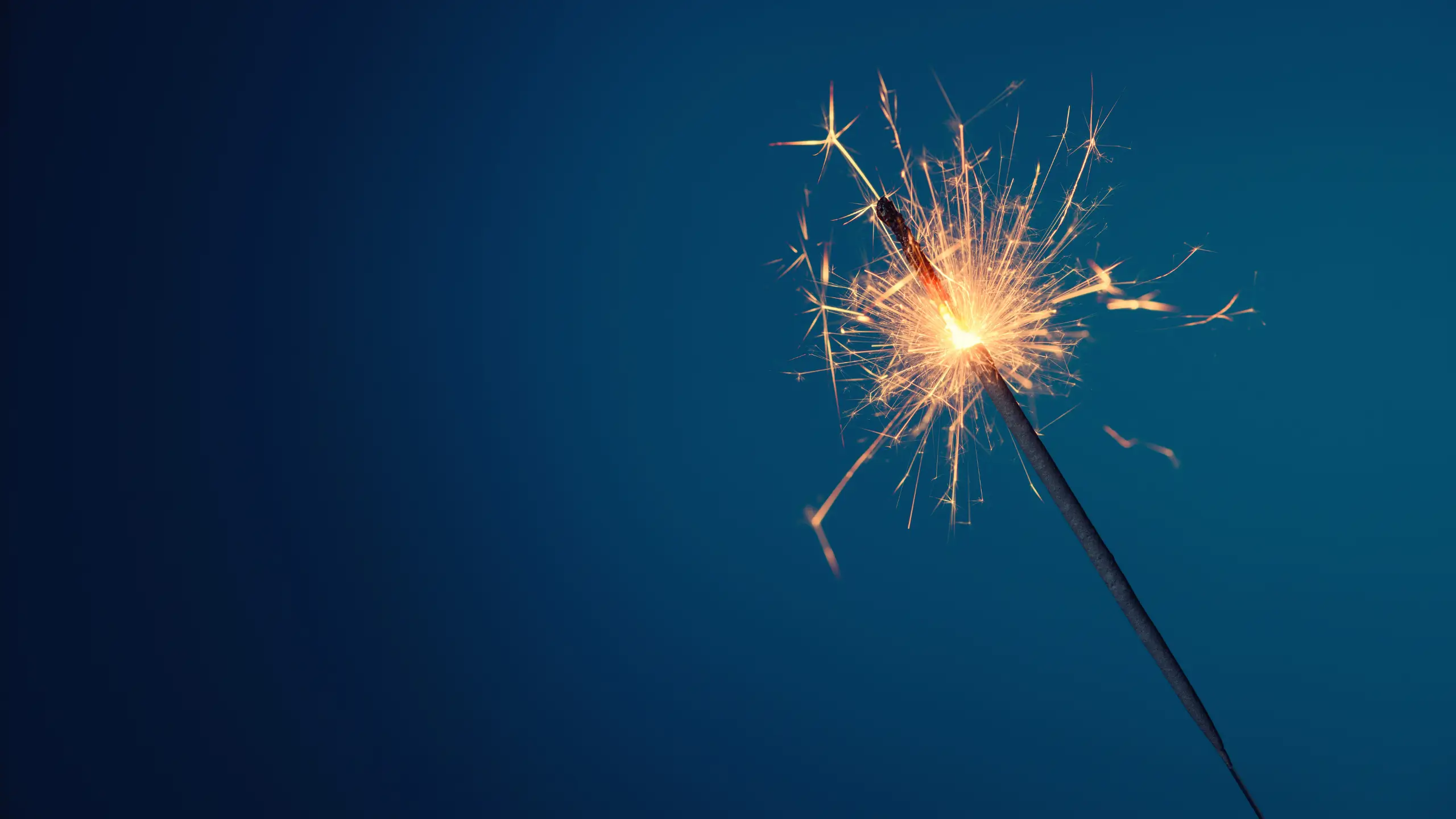A lit sparkler against a dark blue background.