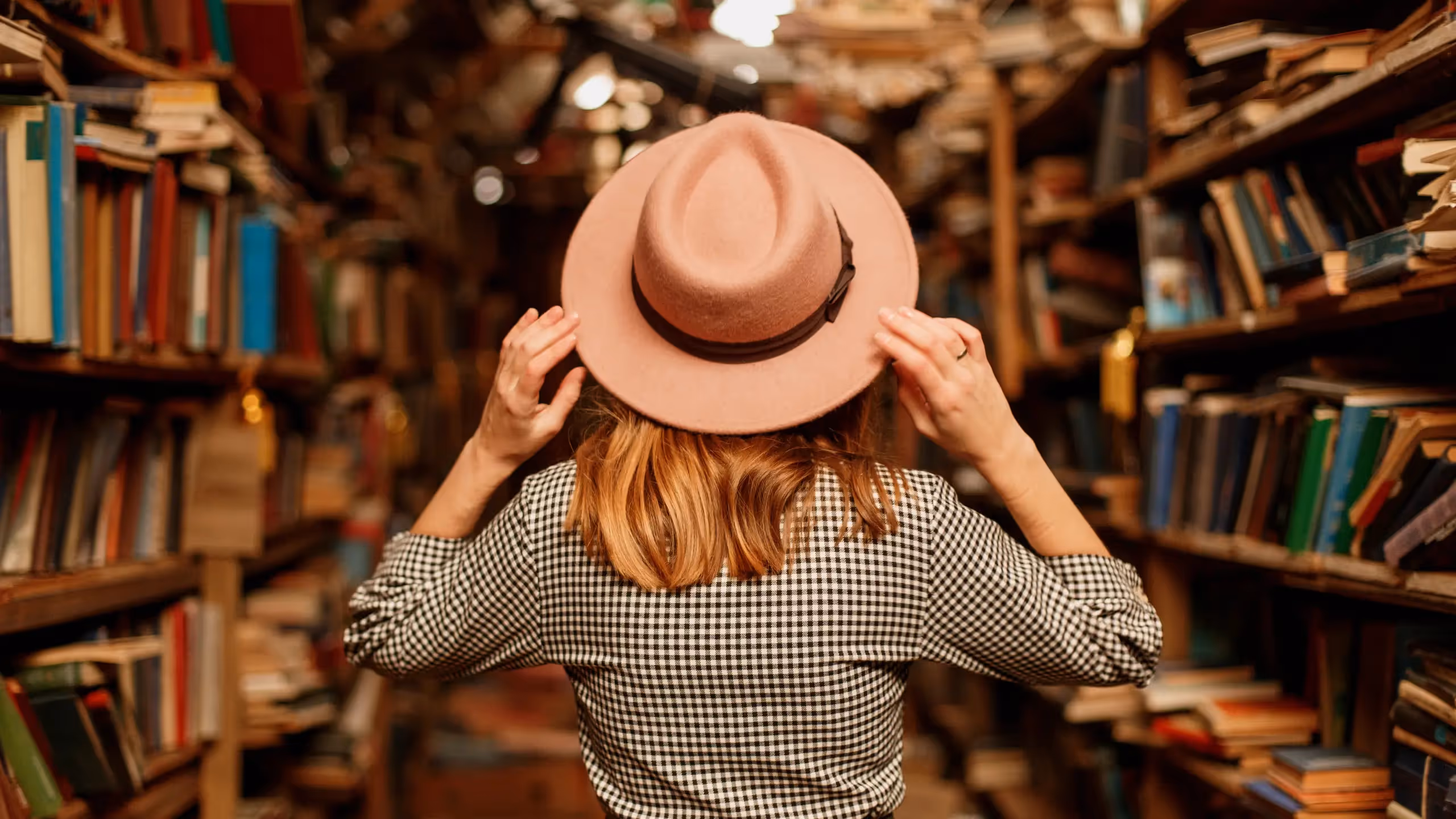 A woman wearing a straw hat stands in a bookshop.