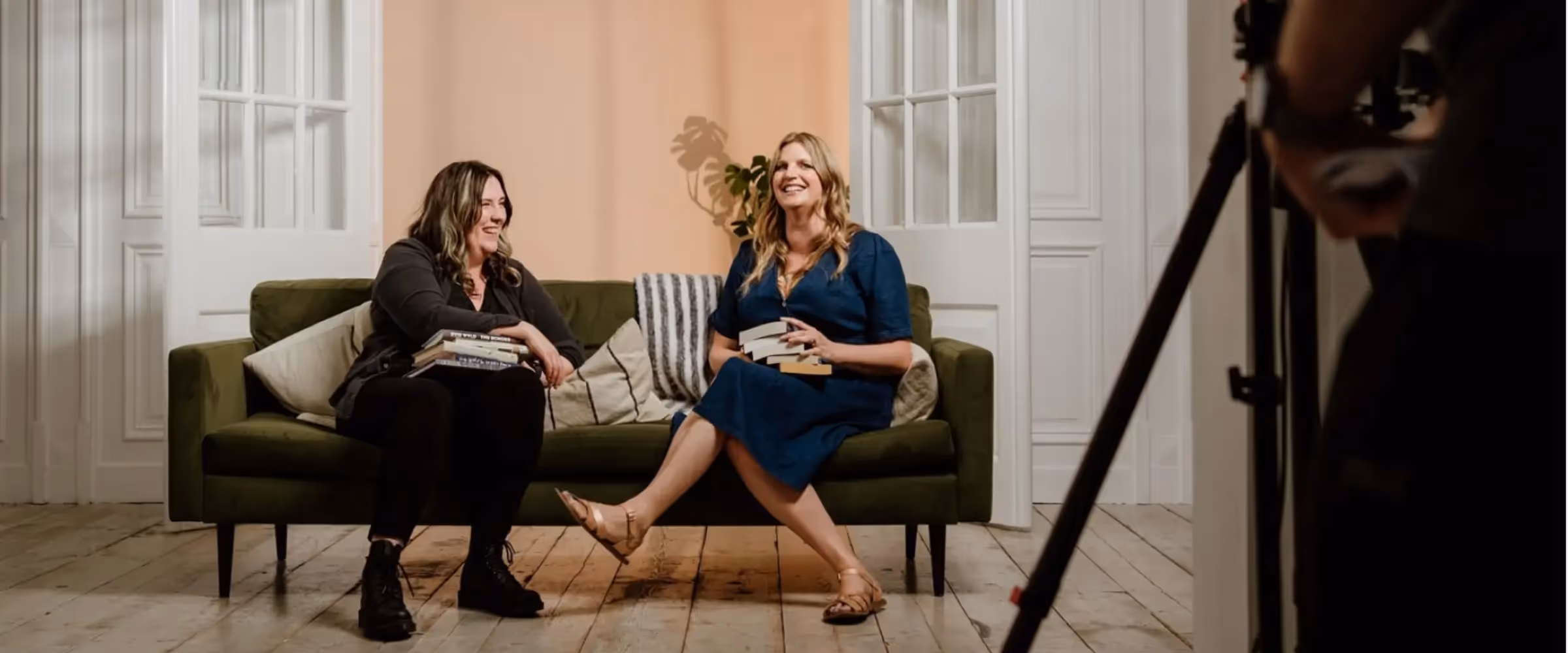 Authors and writing coaches at The Novelry, Evie Wyld and Emylia Hall, sit on a couch in a photography studio.