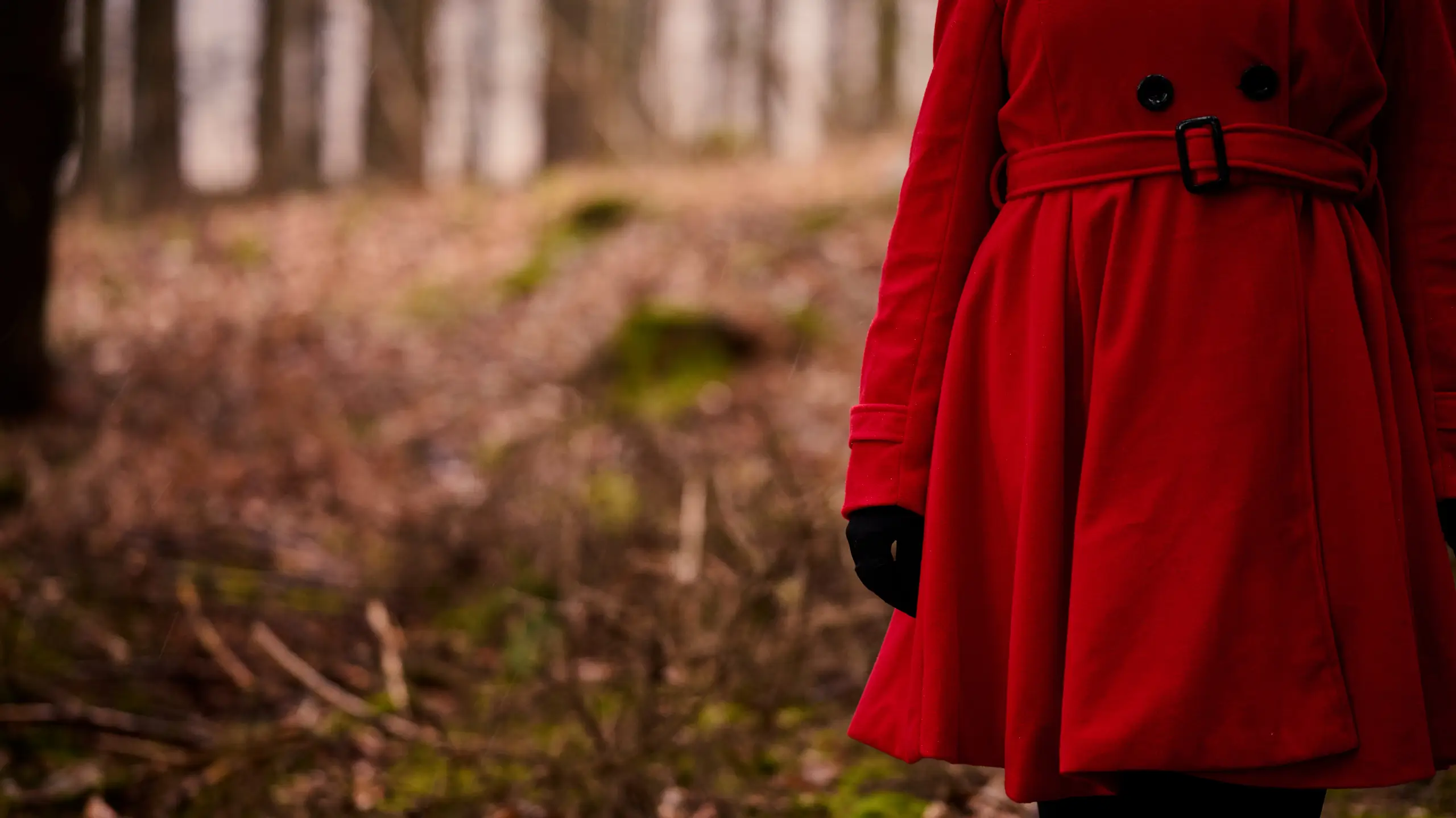Partial view of a woman in a forest wearing a belted red coat.
