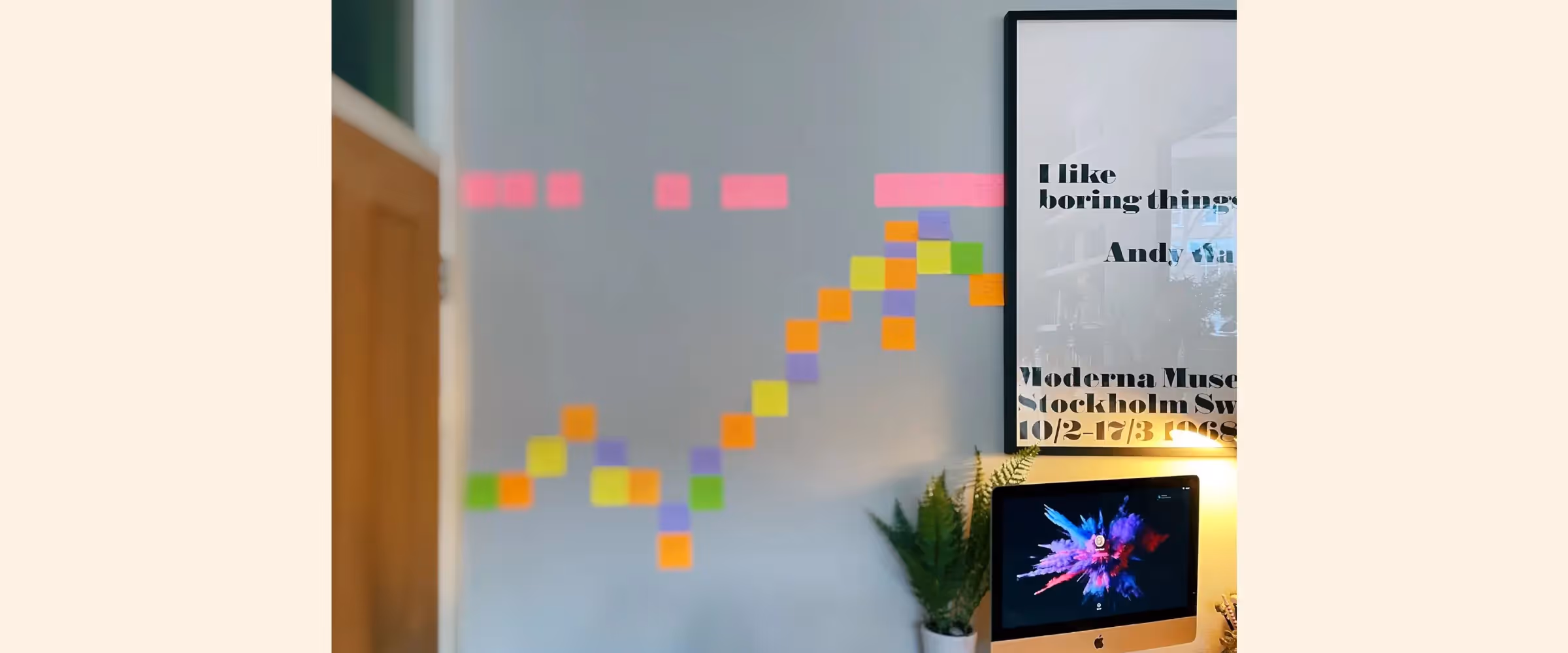 A pattern of colorful Post-it notes stuck to a wall between a door and an Andy Warhol poster.