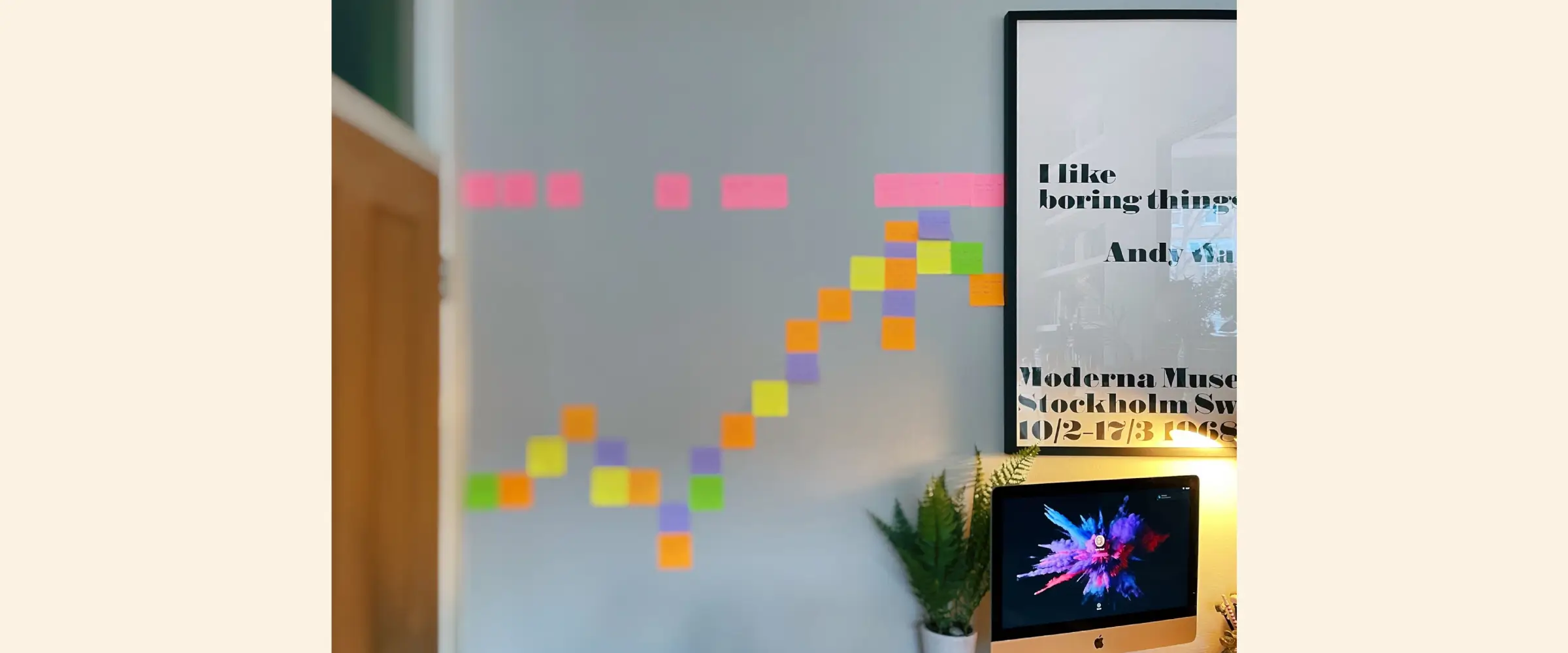 A pattern of colorful Post-it notes stuck to a wall between a door and an Andy Warhol poster.