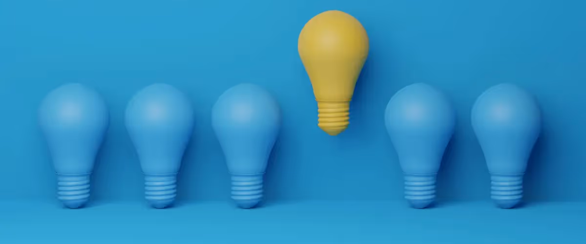 A row of blue lightbulbs against a blue background, with one yellow lightbulb raised above the row.