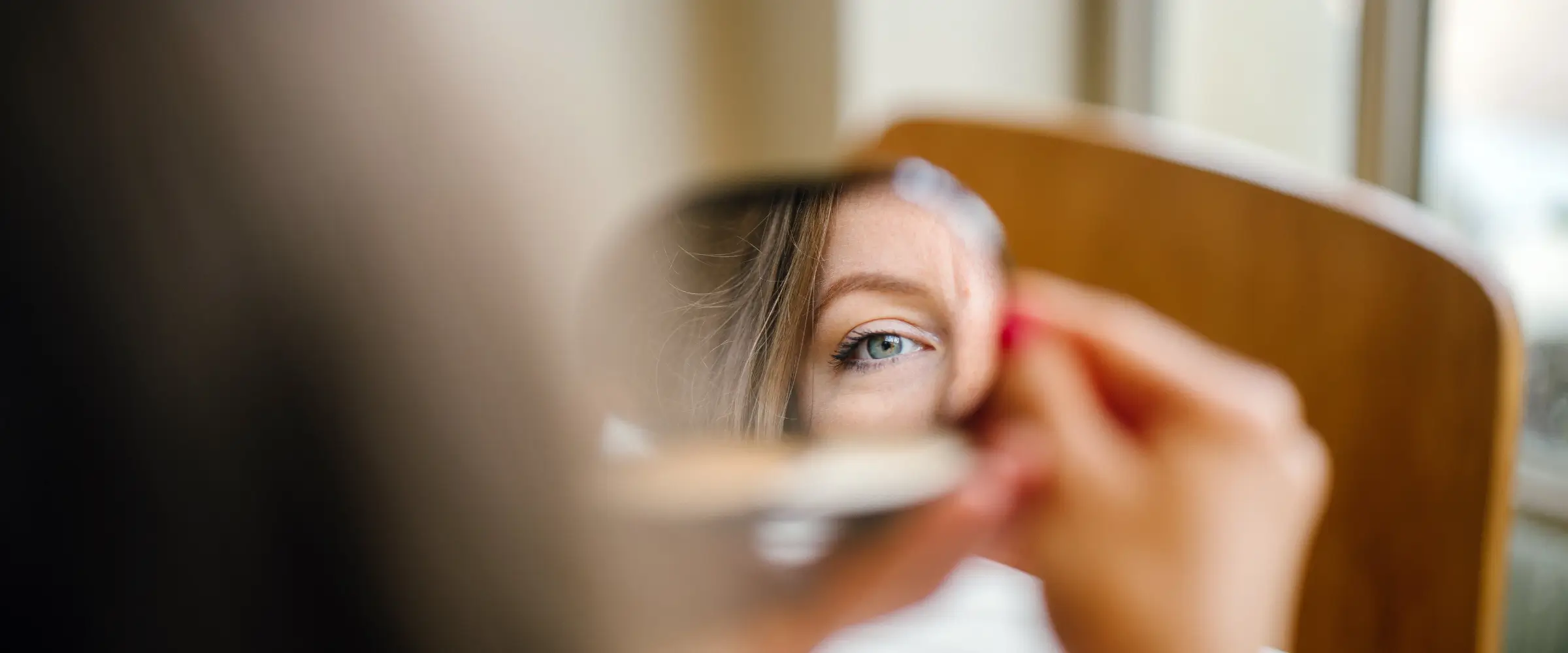 A rear aspect view of part of a woman's face reflected in a small mirror.