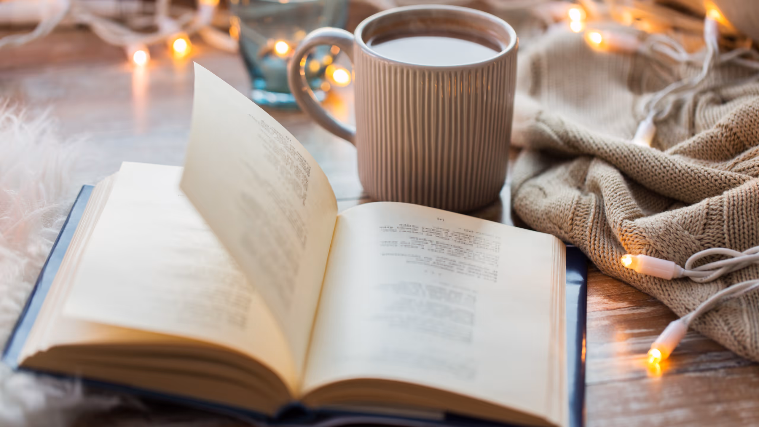 A book lying open beside a cup of cocoa and a blanket.